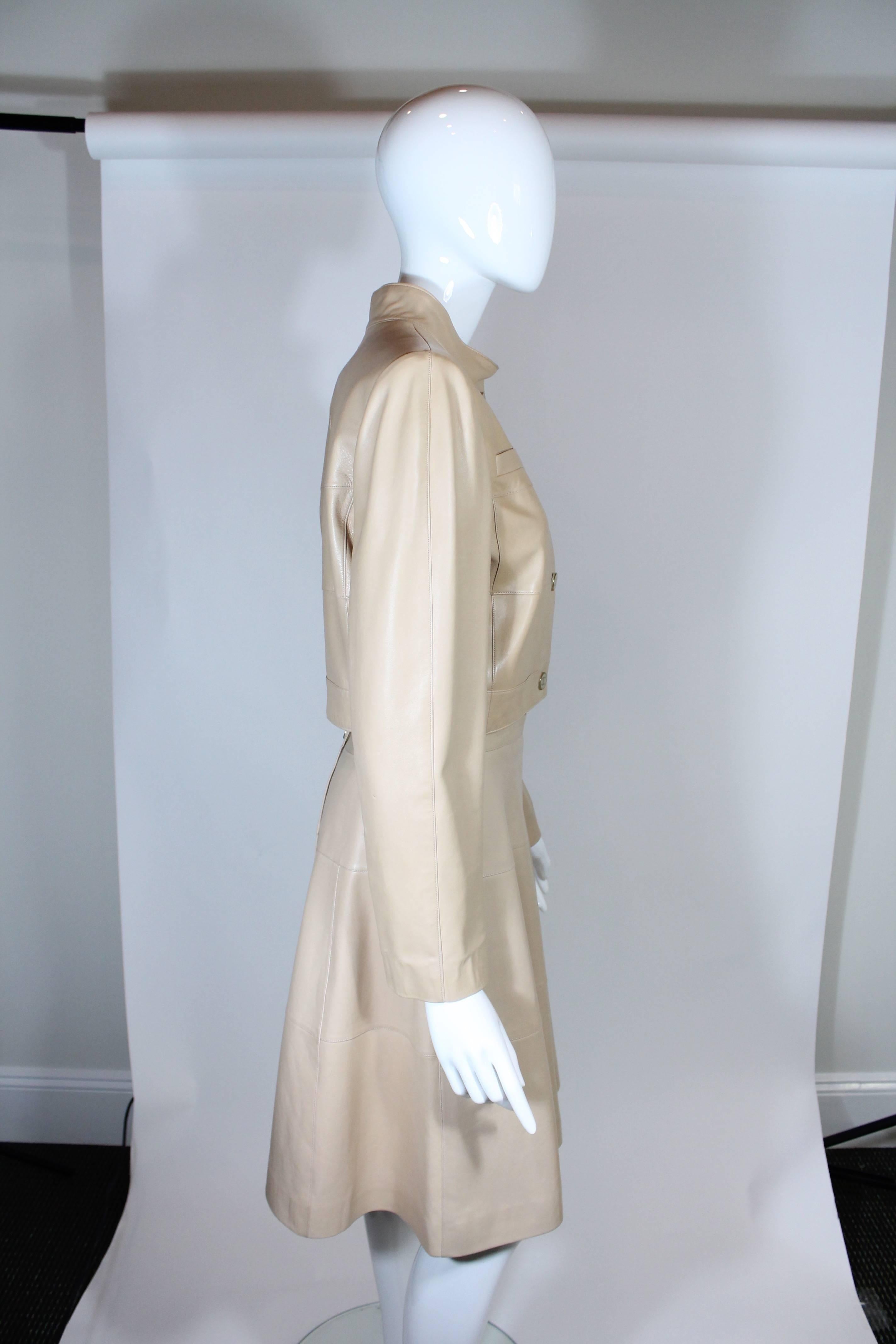 Chanel shows us the ultimate two-piece skirt suit in rich camel leather lined in camel silk. Cropped leather jacket with mock neck collar, four 'CC' buttons, two closed upper pockets. 
A line skirt with back zipper and button.
100% Lambskin
Lining: