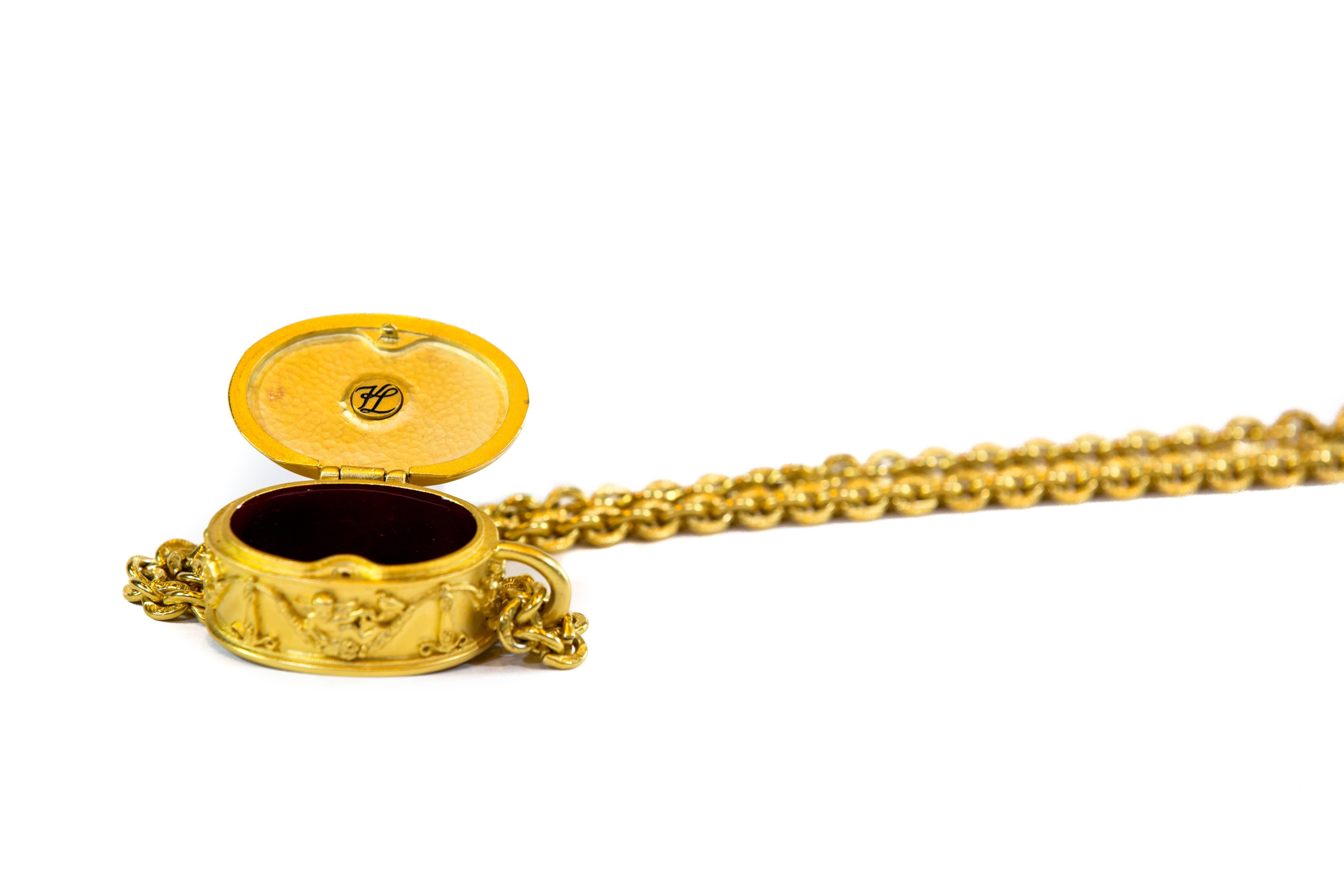 Go vintage chic with this pill box necklace from Karl Lagerfeld. Oval gold tone pill box with cherub handle on top. Burgundy enamel interior with  KL initials. Carved cherub around the outside and signed also on the bottom KL. The chain has etched