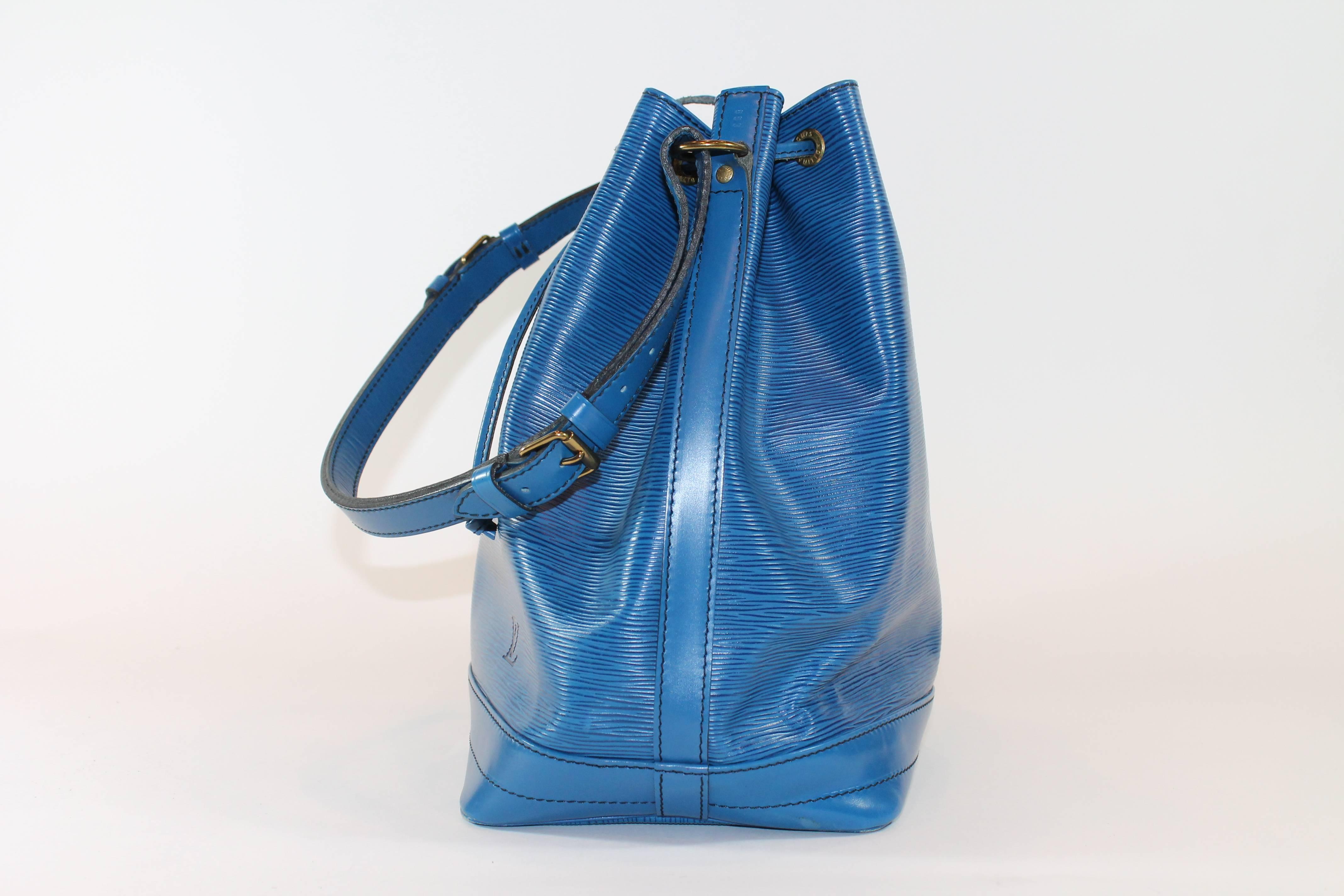 The Louis Vuitton bag is in cyan styled in Epi leather. This bag has brass hardware with an adjustable flat shoulder strap. It includes a drawstring closure at top. One interior pocket with zipper closure.