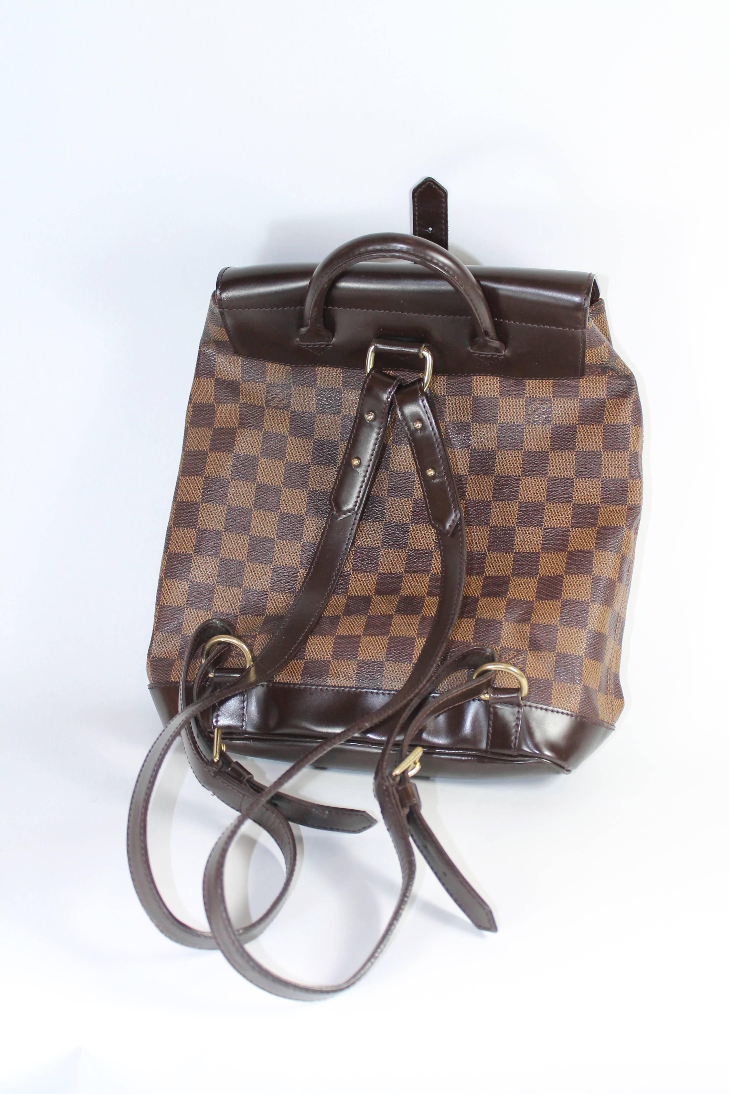 Brown and tan Louis Vuitton Damier coated canvas Soho backpack with brass hardware. Includes adjustable shoulder straps, single rolled top handle, interior wall pocket and front buckle closure.