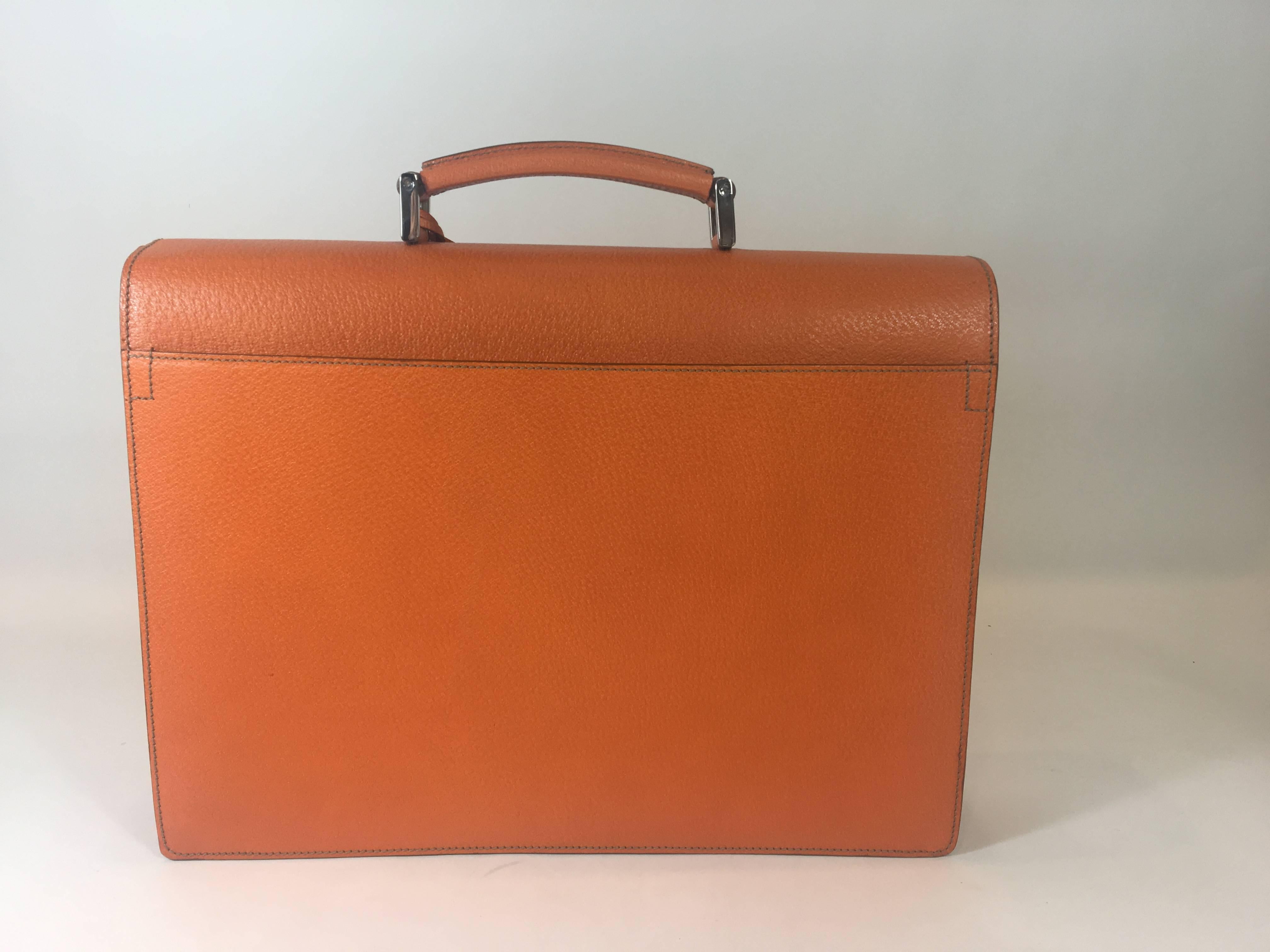 This briefcase is orange cinghiale leather. It has one rolled handle and silver tone hardware. Includes a flap top with a pinch clasp closure. The interior is done in taupe leather, featuring dual compartments. The front compartment features one