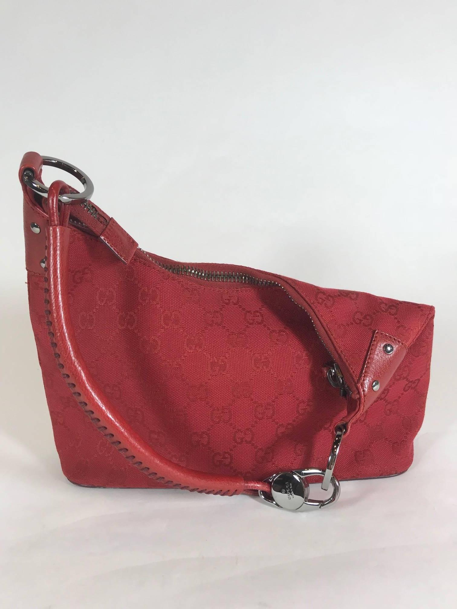 This Gucci GG canvas hobo bag is fabulous in radiant red. Features include red canvas monogram, red leather bottom and trim, and silver metal hardware. Top zipper closure. A rolled shoulder strap attaches to the bag by two metal rings with one side