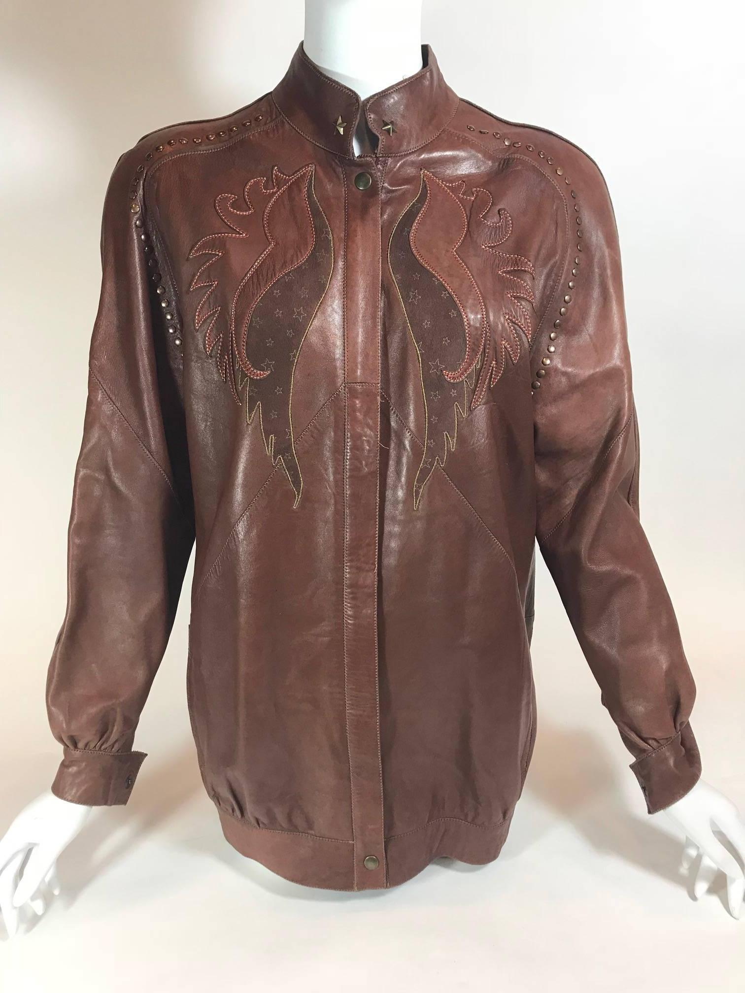 Brown leather. Bronze hardware. Zipper closure with single button at top and bottom. Front design featuring star pattern and tan and red stitching. Mock neck collar with star stud on each side. Flat stud detail along shoulder and arm seam. Star and