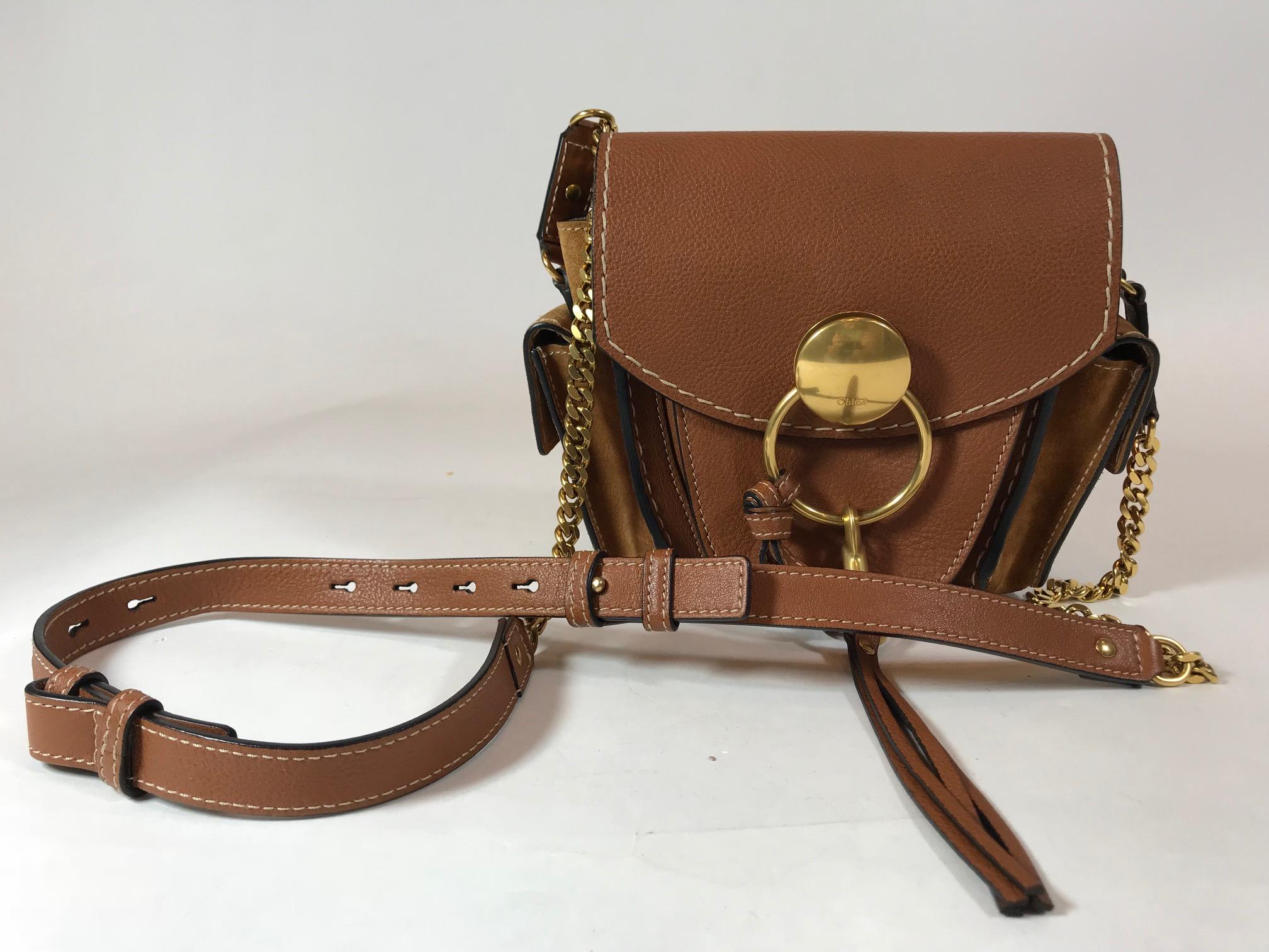 Brown grained leather. Gold-tone hardware. Magnetic snap closure at front flap. Tonal suede accents. Adjustable flat shoulder strap with chain-link accents. Dual exterior pockets with magnetic snap closures. Single slit pocket at flap underside.
