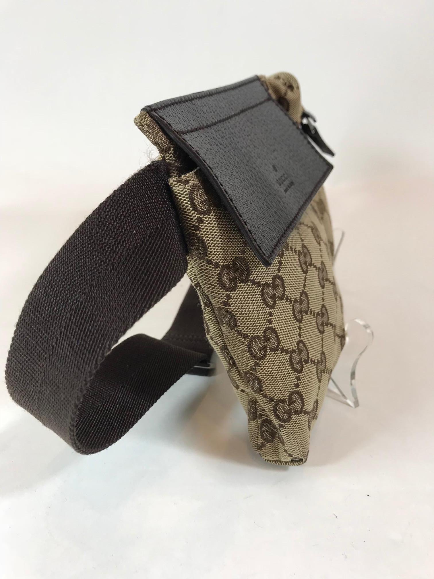 Beige and brown GG canvas Gucci waist bag with gunmetal hardware, single canvas waist strap with buckle closure, chocolate leather trim, dual exterior pockets; one with zip closure, chocolate woven lining and zip closure at back.