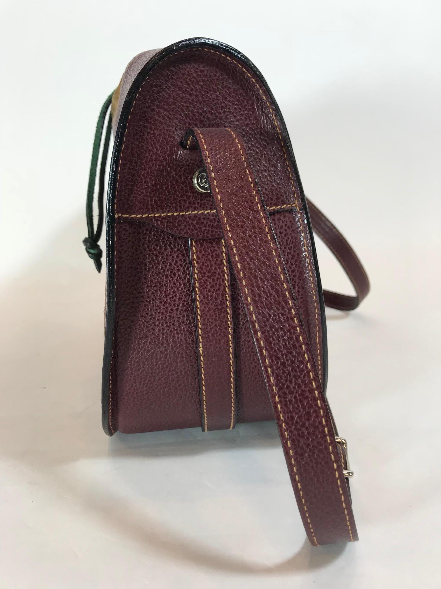 Dark burgundy leather with tan suede top. Silver-tone hardware. Green suede drawstring closure. Green leather bullet holster strap along front of bag Adjustable shoulder strap. Tan suede interior. One interior zippered pocket.