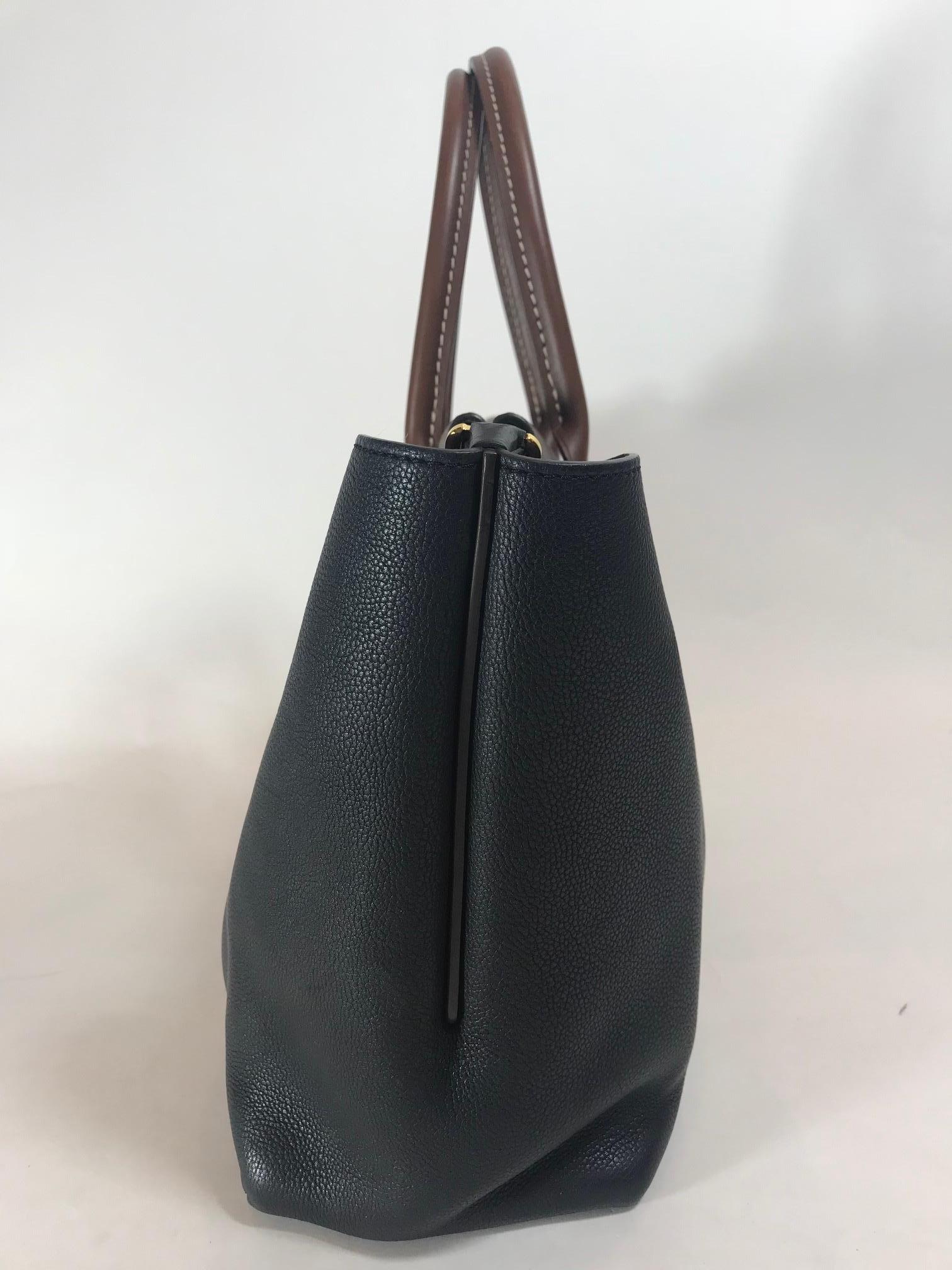 The leather piping trim matches the golden brown rolled leather top handles. The expansive sides of this W-shaped bag can be worn wide or tucked in and snapped inwards. The top is secured with hidden magnet closures, and opens to a light brown suede