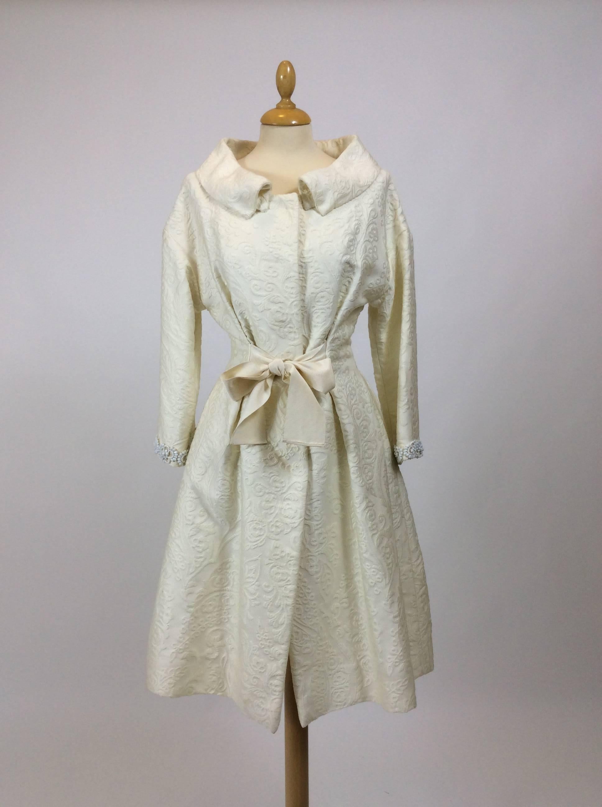 This lovely Giambattista Valli overcoat is in a white ivory brocade cotton and silk  fabric.It has snaps closure, 3/4 sleeves with embroidered beadeds hem sleeves, round collar and grosgrain waist sash.It has two sides pockets and pleateds