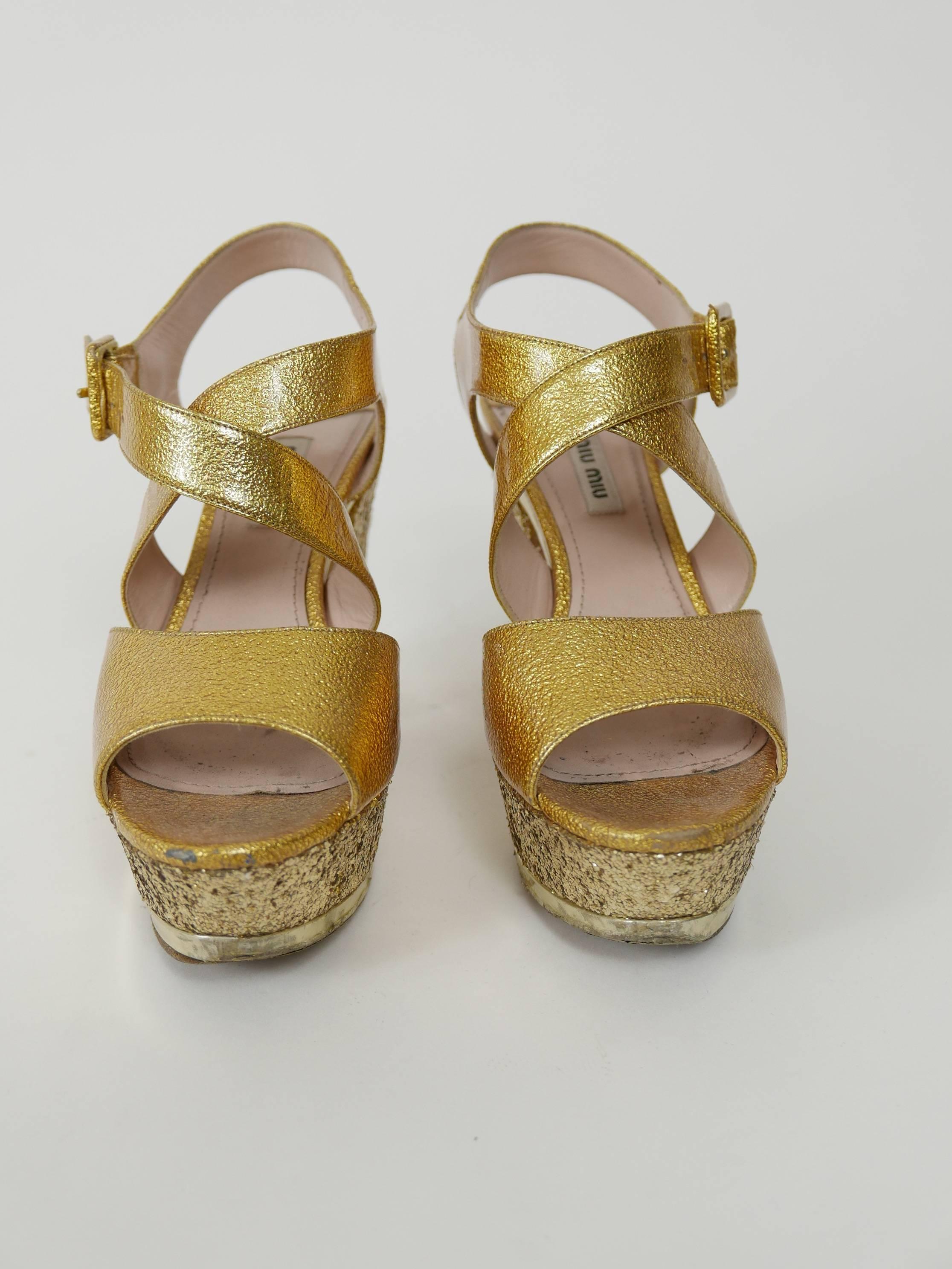 These feminine and gorgeous Miu Miu sandals are in golden patent leather with gold glitter covered heels and platform. They have buckle closure at ankle straps. 

Very good condition.

Brand: Miu Miu - Made in Italy 
Material: