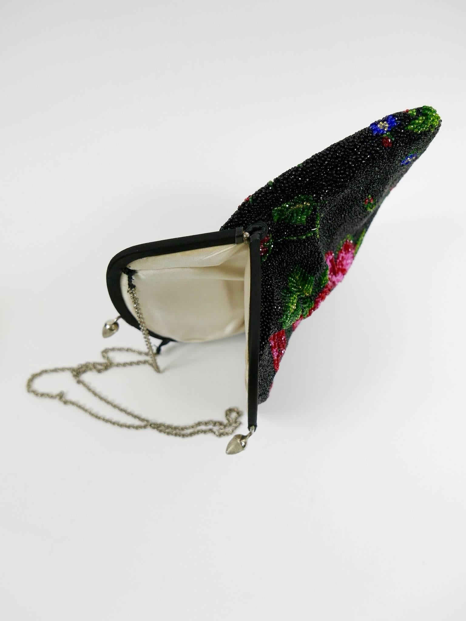 This gorgeous 1950s evening bag is all entirely hand-made with black glass beadeds and adorned with bright and colorful embroidered floral details. It has silver metal handle chain and closure, is lined with cream satin and has a little pocket