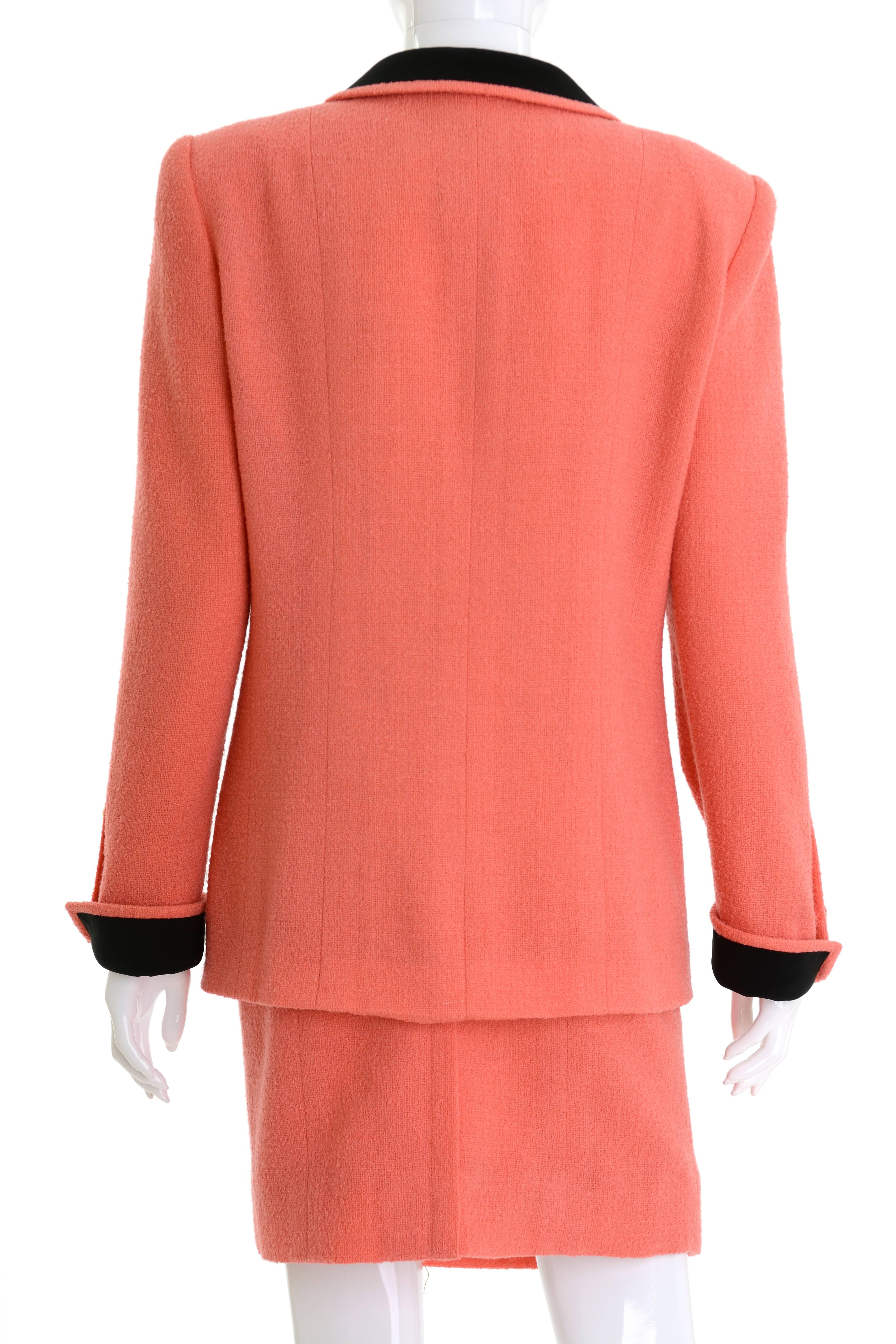 This adorable and authentic Chanel suit dress is in a coral pink boucle wool fabric with black details. The jacket has shoulder pads, two front little pockets and closing with CC logo golden metal buttons. The pencil skirt has back zip closure with