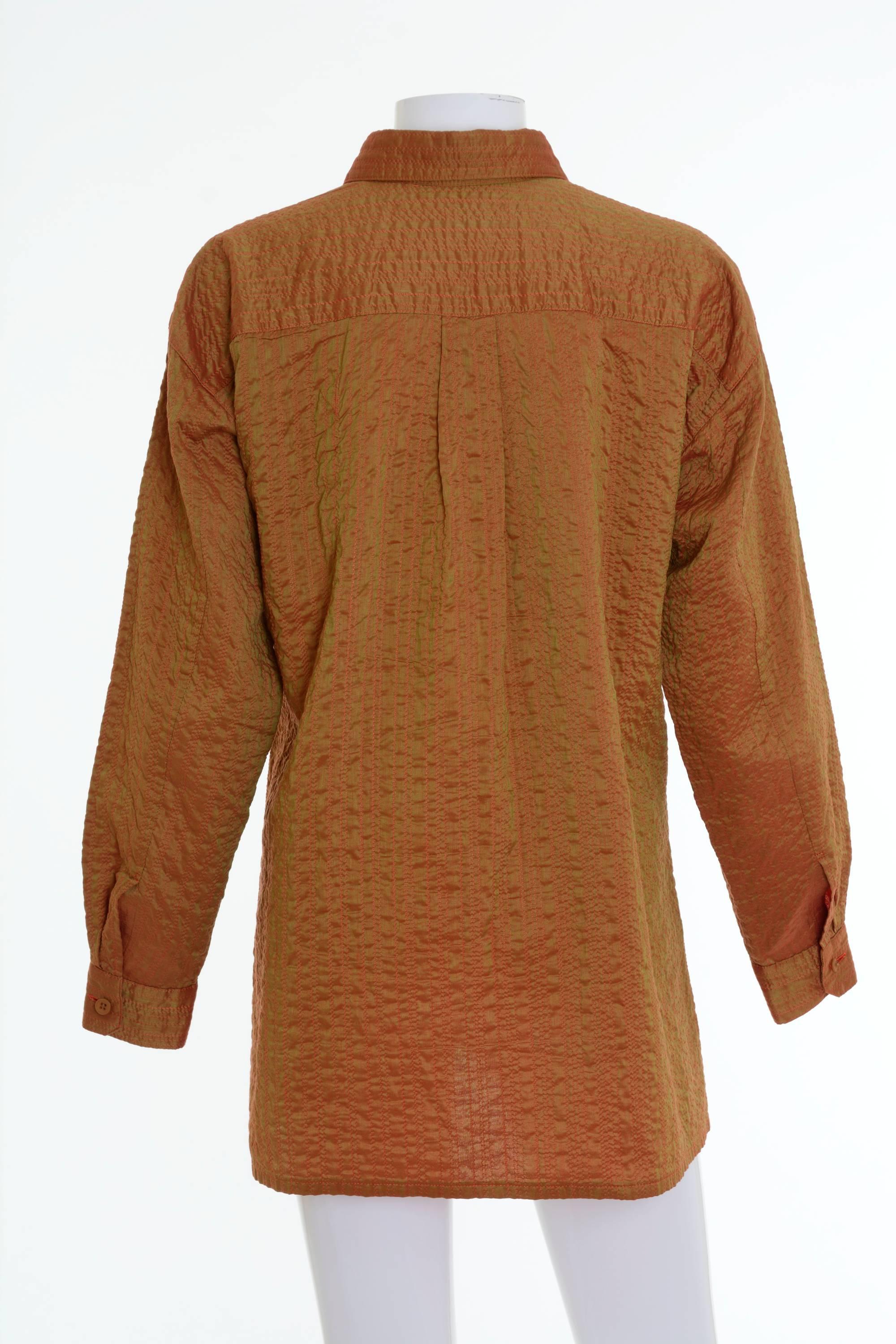 This lovely Issey Miyake shirt is in a rust base fabric with gold-clor design stamped on it that makes it appear like a copper color and orange stitching and interior. It has long sleeves, side vents and one frontal pocket. 

Excellent vintage