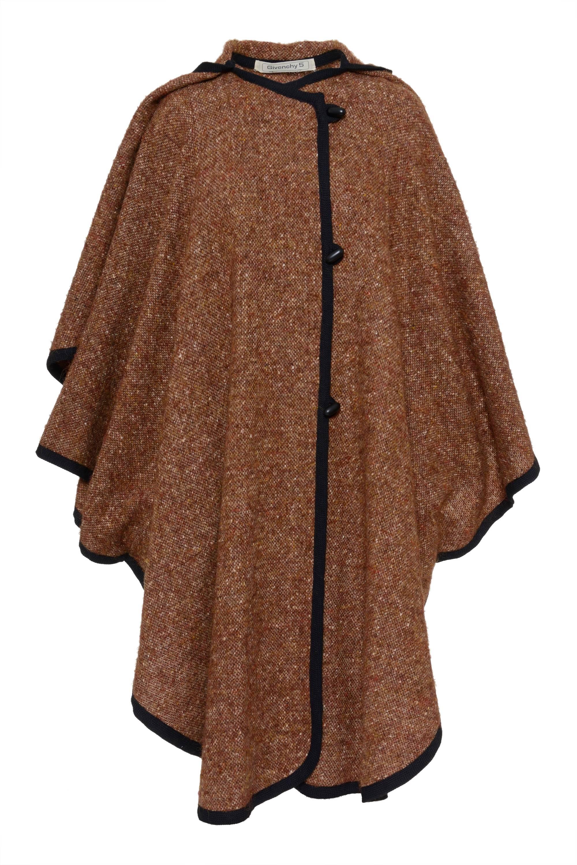 This 1980s beautiful brown weave wool cape by GIVENCHY 5 has a black hem, circular neckline, two front seam pockets hidden in a long dart for adapt it to the body shape, button and loop closure, and a little cape over with a decorative tassel. Made