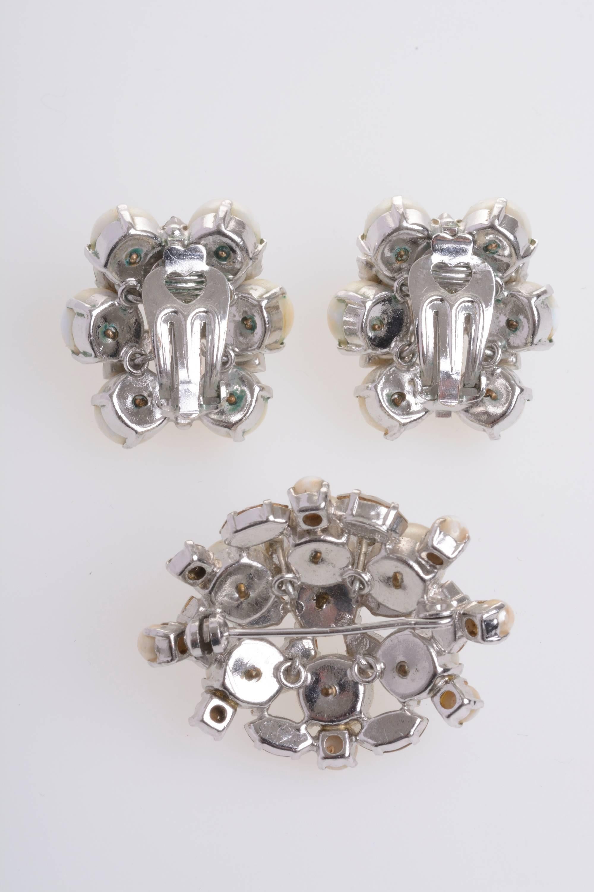 This gorgeous vintage set of earrings and brooch by DIOR has white ivory pearls and silver gems doing a floral shapes: the brooch has a oval shape made by 6 little pearls and 8 gems more around the flower, the earring have circular floral shape and