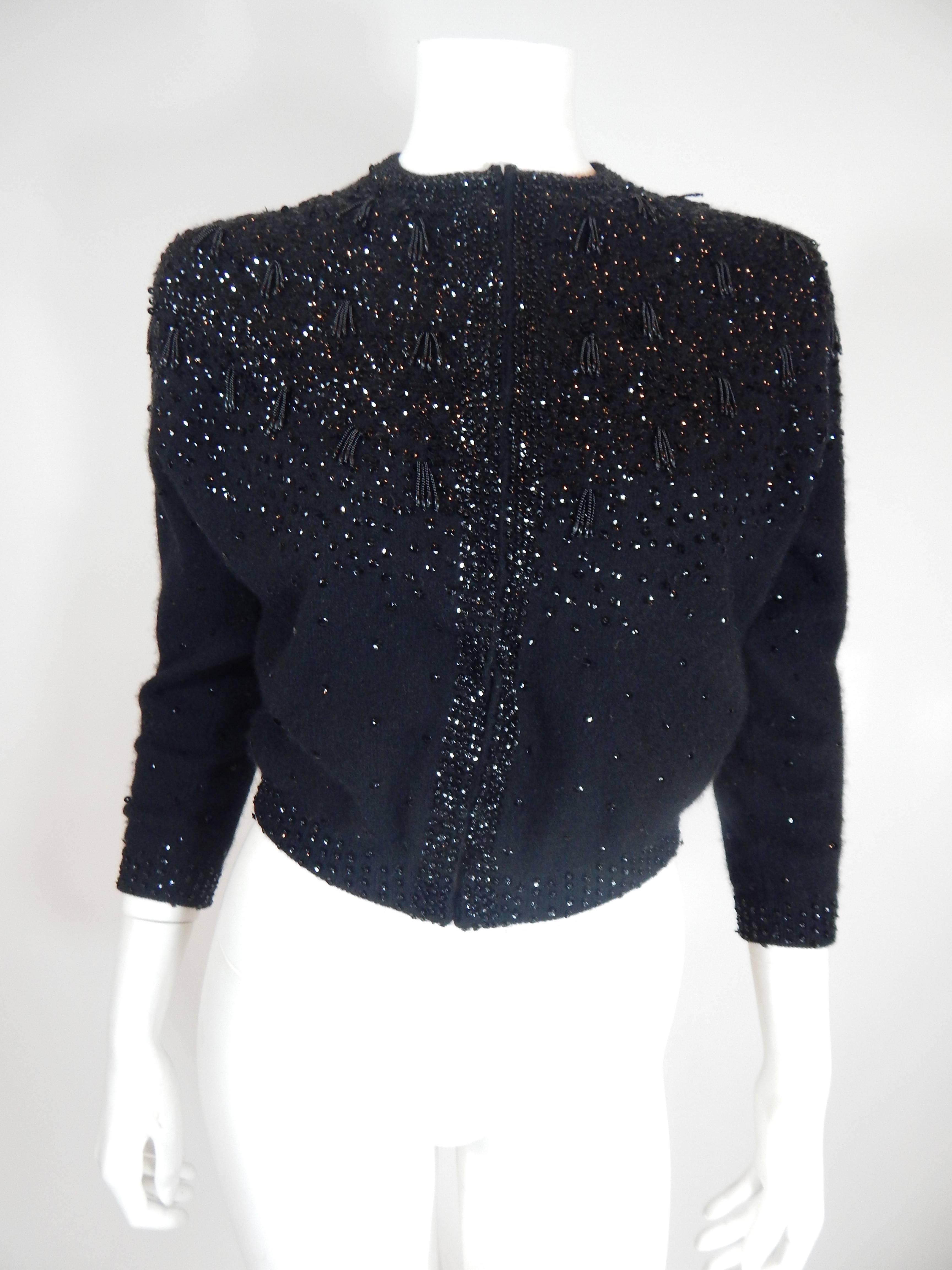 1950s Beaded Sequin Cardigan Sweater. Hand decorated and Made in Japan. Black sweater, beads, fringe beads and sequin. Entire piece is black. Hook and eye front closures. 70% Lambswool, 20% Angora, 10% Nylon. Excellent Condition. Siz e Tag reads 38.