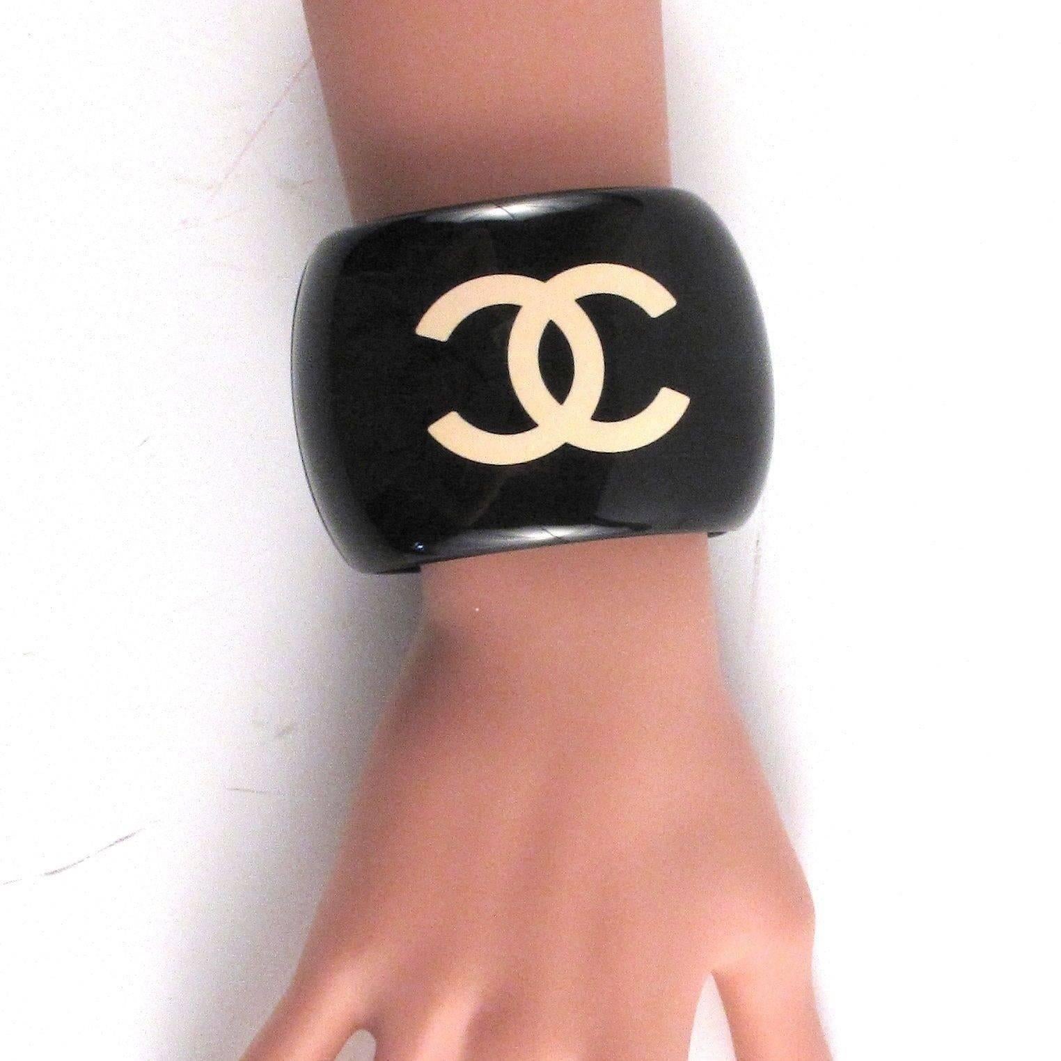 Chanel - Cuff Bracelet

Color: Black / White

Material: Resin

------------------------------------------------------------
 
Details:

- CC logo at front

- camellia motif at back

- gold tone hardware

- stamped 05P

- item #