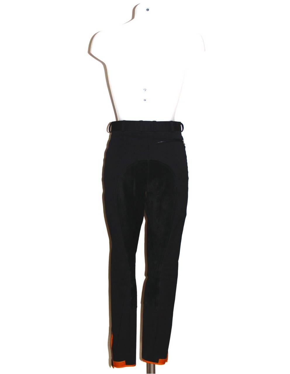 Elegant Hermès black stretch cotton jodhpur pants featuring black suede at inseams, three zippered pockets with stirrup zipper pulls (two front, one back), hook-and-eye/zip fly and snap front button closure and orange scratch closure at ankle.