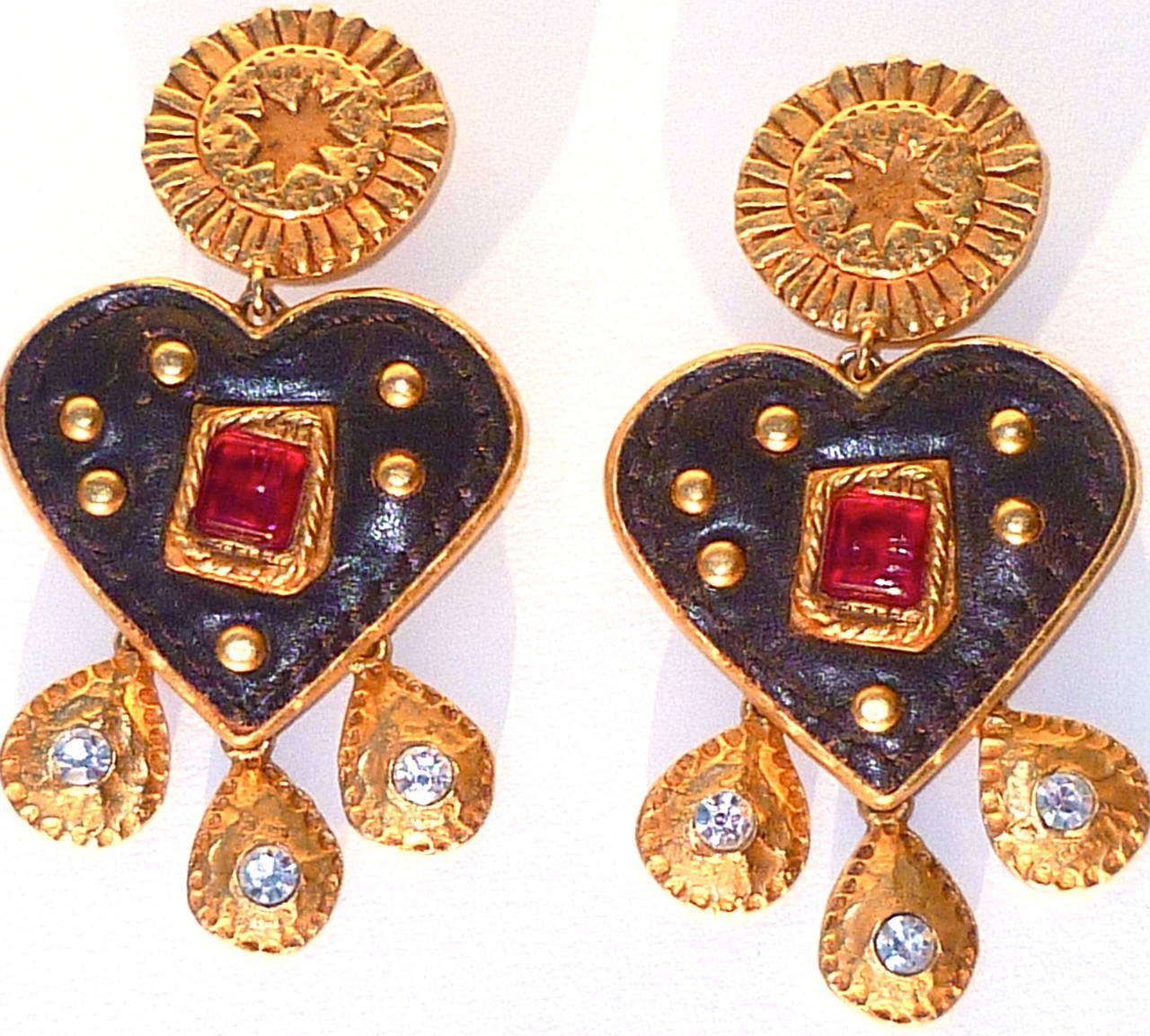 From the Winter 1990 Christian Lacroix Collection, these large dangling ear clips are made in three articulated sections - the ear clip as a large gilt sun (or sunflower), hung with a brown leather heart  with a red poured glass center framed in