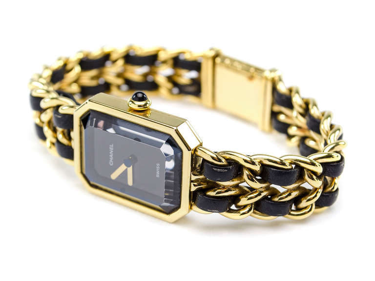 Gold plated Chanel Premiere watch with octagonal case, black dial, gold sword hour and minute hands, faceted onyx cabochon crown, chain-link bracelet, black leather trim, faceted crystal sapphire, Swiss quartz movement and tab insert closure.