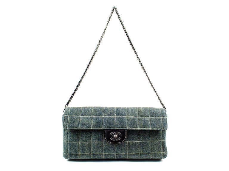 Perfect for summer! This Chanel denim east wast flap features square detailing with ivory stitching, brown leather details on front flap, silver tone interlocking CC hardware. Interior features two pouch pockets.