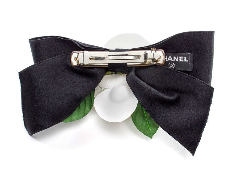 Make a statement in this Chanel hair pin! This hair clip features a large white silk camellia flower, green leaf details and black ribbon. Clips into the hair.

Measurements: 7.5