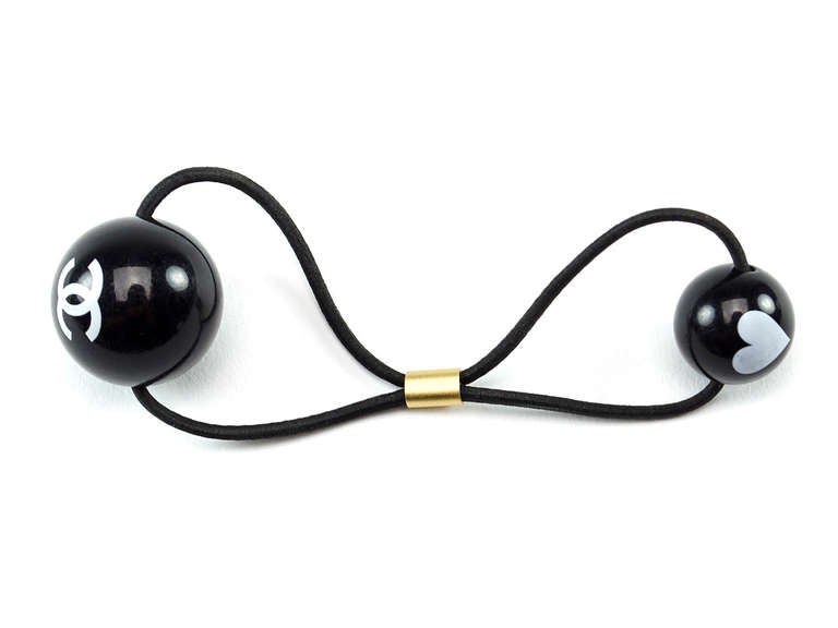 Whip your back with this chic Chanel hair tie! Hair tie features black ball with white interlocking 'CC' logo with a smaller black ball with white heart, just darling!

Includes: Box.