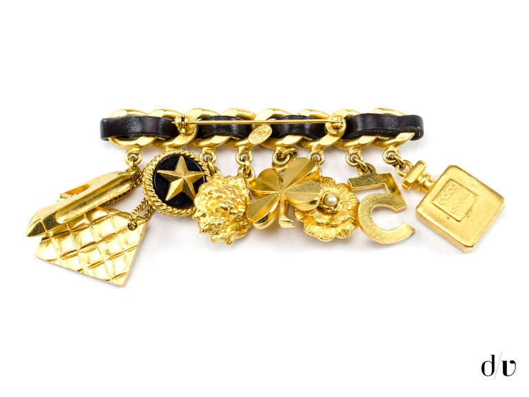 Extremely rare! Chanel vintage brooch with braided black leather detail and gold tone hardware. Charms include a Coco Chanel perfume bottle, Number 5, Camellia flower, Four leaf clover, Lion head, Star, Handbag & High heel.

Includes: