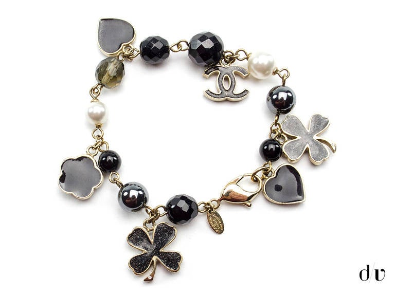 We love this Chanel charm bracelet featured in black enamel detail on silver tone hardware. This charm bracelet features four leaf clover, interlocking 'CC' charm detail, heart, camellia flower detail and beaded detail. Hook closure. Made in