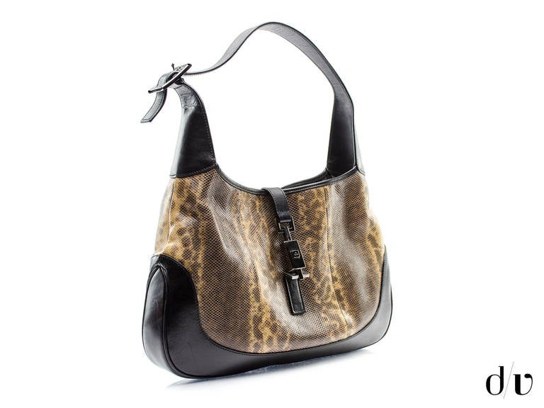 Take a step back in time in this chic Gucci Jackie hobo shoulder bag. Featured in lizard skin this bag will stand the test of time for years to come. Features black leather trim throughout, beige and brown lizard skin details. Interior features one