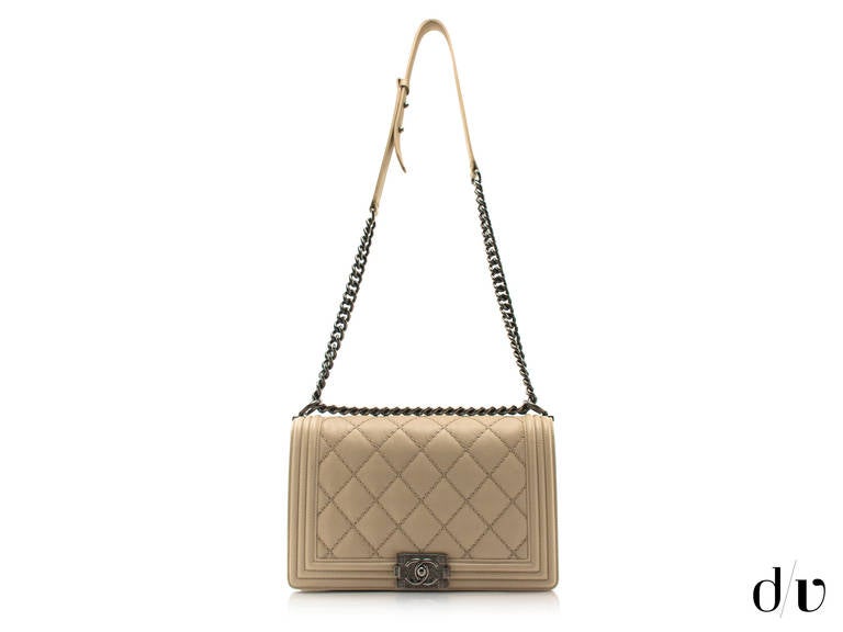 Very Chic! This exquisite, soft to touch lambskin boy bag from Chanel comes in a rich beige tone color. Classic chevron pattern features large stitching. Edges of the flap and the back a re decorated with three-tier piping. Rustic hardware includes