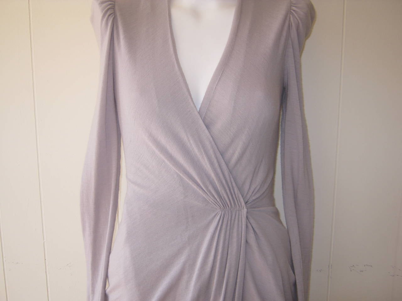 Grey with a hint of purple, this deep v-necked, long sleeved light wool with 5% lycra dress features a wrap front with press stud and tie fastening, draped sides and gathered detailing on the shoulders. This is a very comfortable and elegant