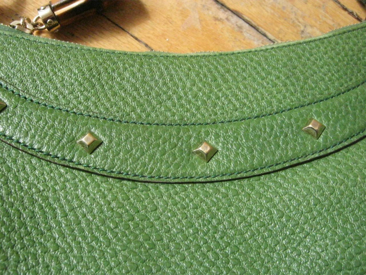 This hobo style Gucci bag made of a beautiful green pebbled leather can be worn for day or evening. There is a line of decorative diamond shaped studs on both sides of the bag and a bamboo handle with a 7