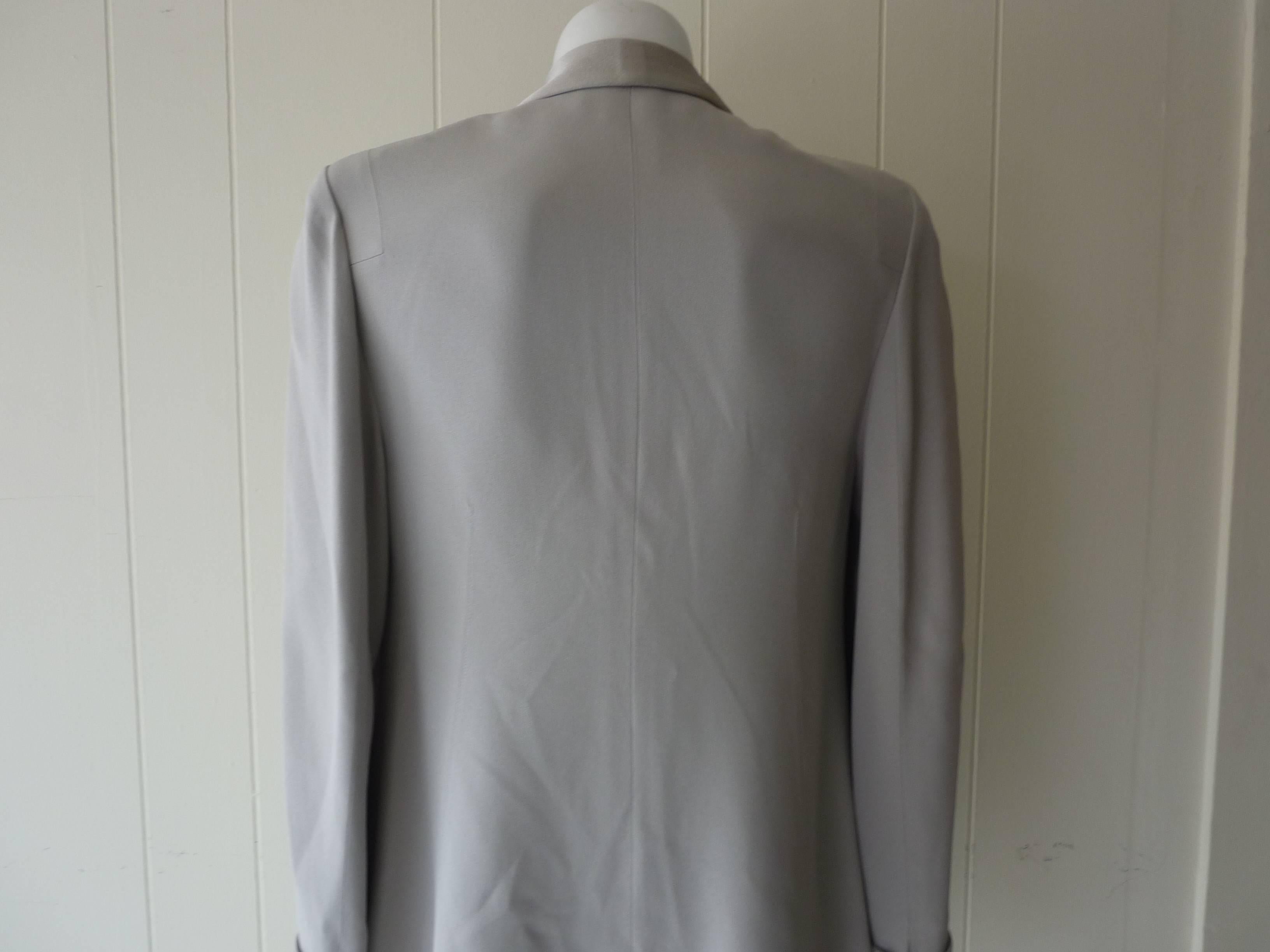 Wonderfully cut jacket in acetate (65%) and Viscose (35%). The soft pearl grey jacket has contrasting shiny lapels and turned cuffs (with slits); one covered button and two flap fake pockets.