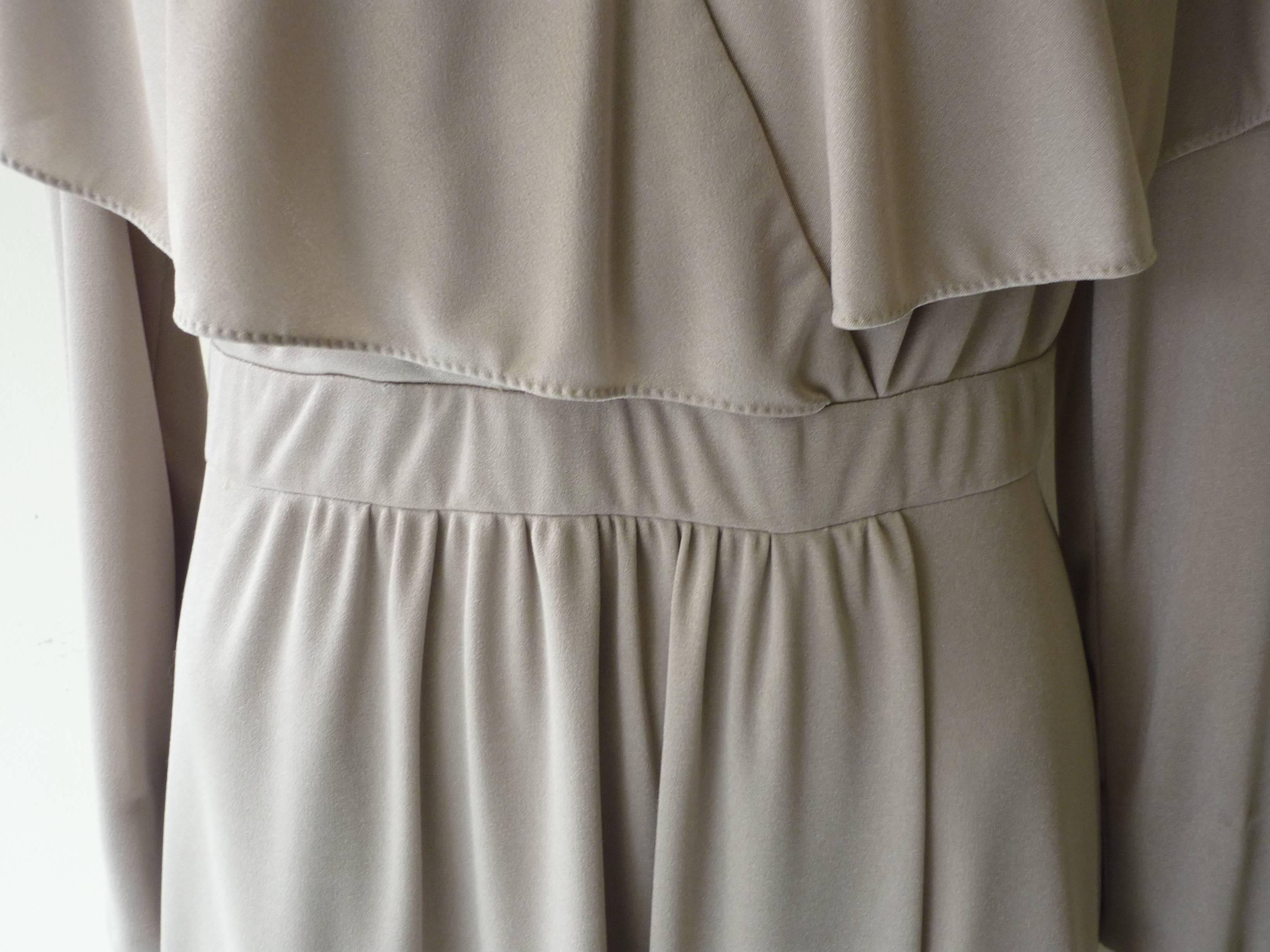 Simple and well cut half wrap dress in shiny beige tones, with a v-neck and a cape overlay. The long sleeves have eight covered buttons each, and there is a built in waist band.

The dress has hand finished elements and a zip closure to the