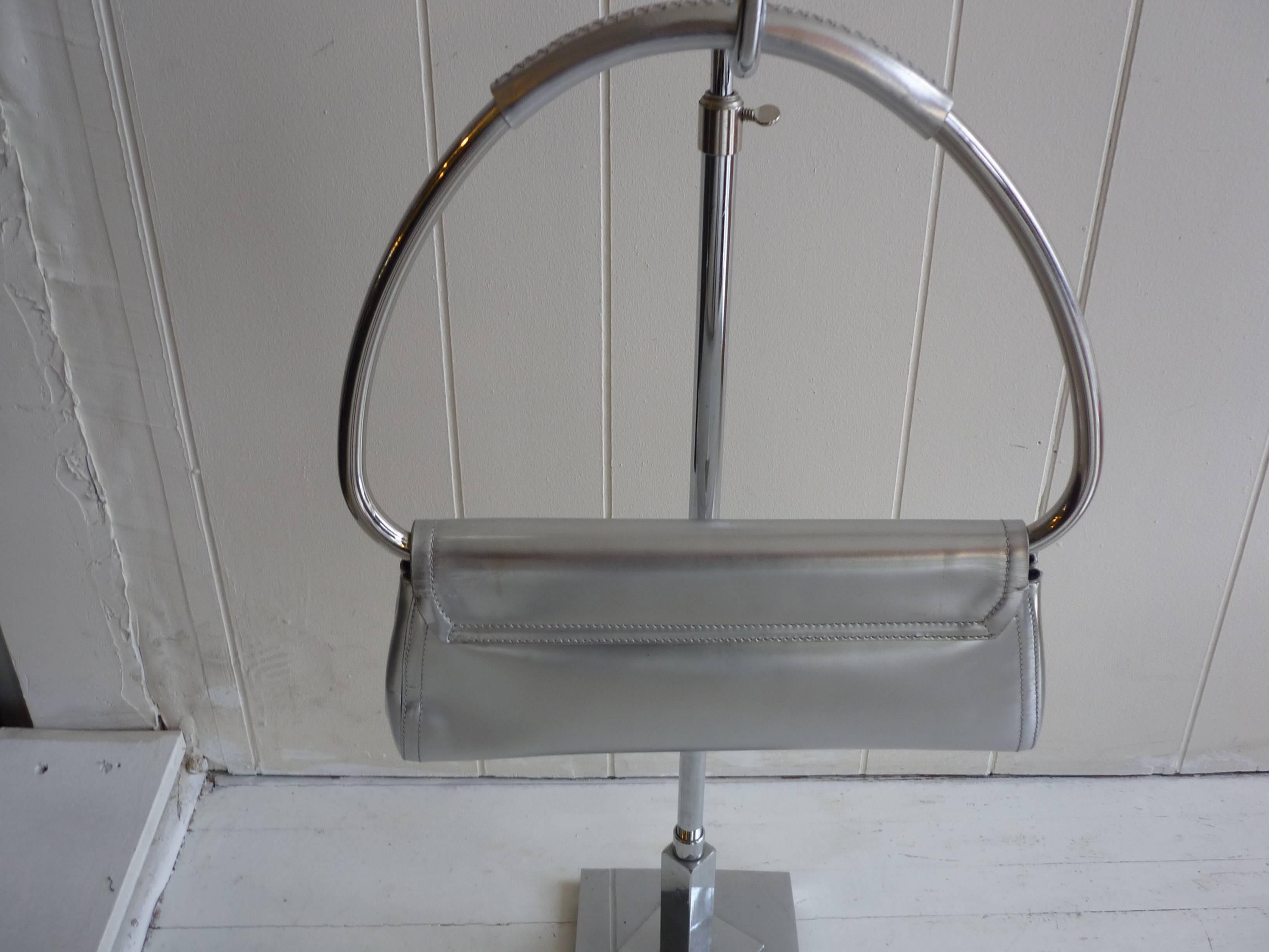 Silver leather bag with silver-tone ring handle. The lining is satin; there is an interior zip pocket; snap front closure, and side snap closures which open to expand the depth of the bag. 

The bag is in overall excellent condition.

The handle