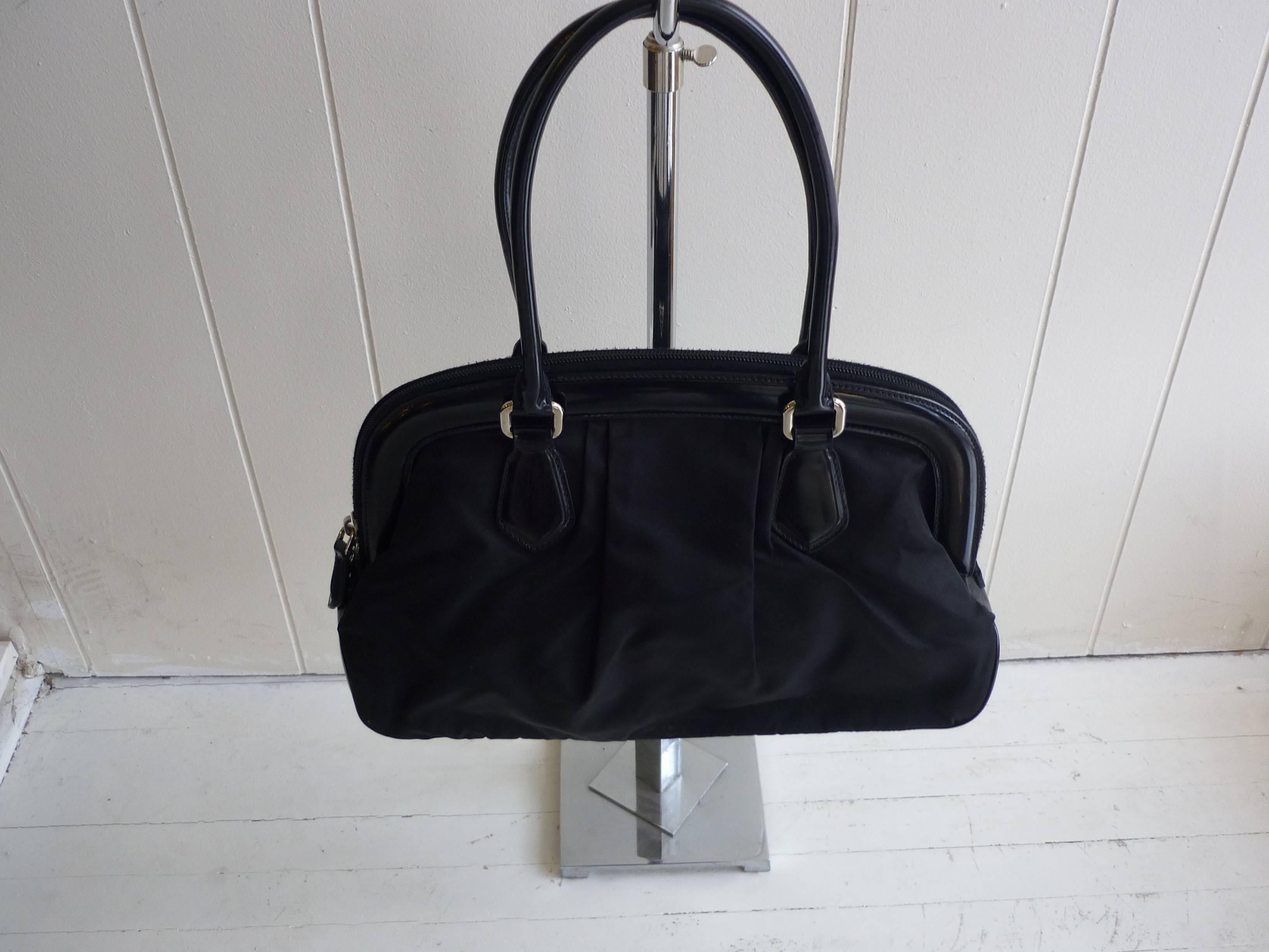 Nice structured frame and top zip closure with two zip pulls, this bag has silver-tone hardware; a triangular Prada logo on the front; black Prada monogrammed lining, and two interior pockets one zip and the other open.

The bag is in very good