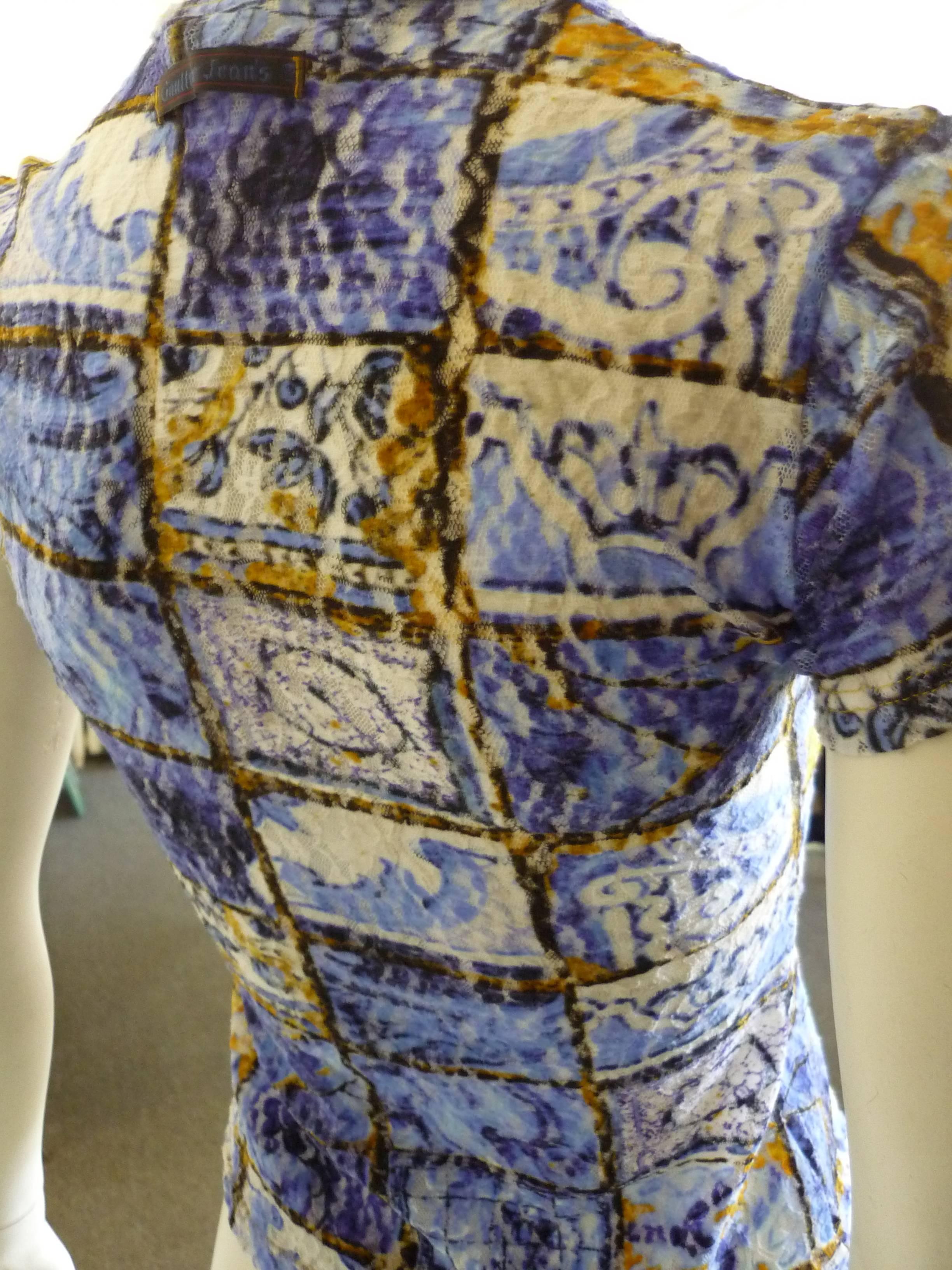 The short sleeved top has a picture frame print with different relief motifs.

The dominant colours are blue white and orange, and the material is polyamide.