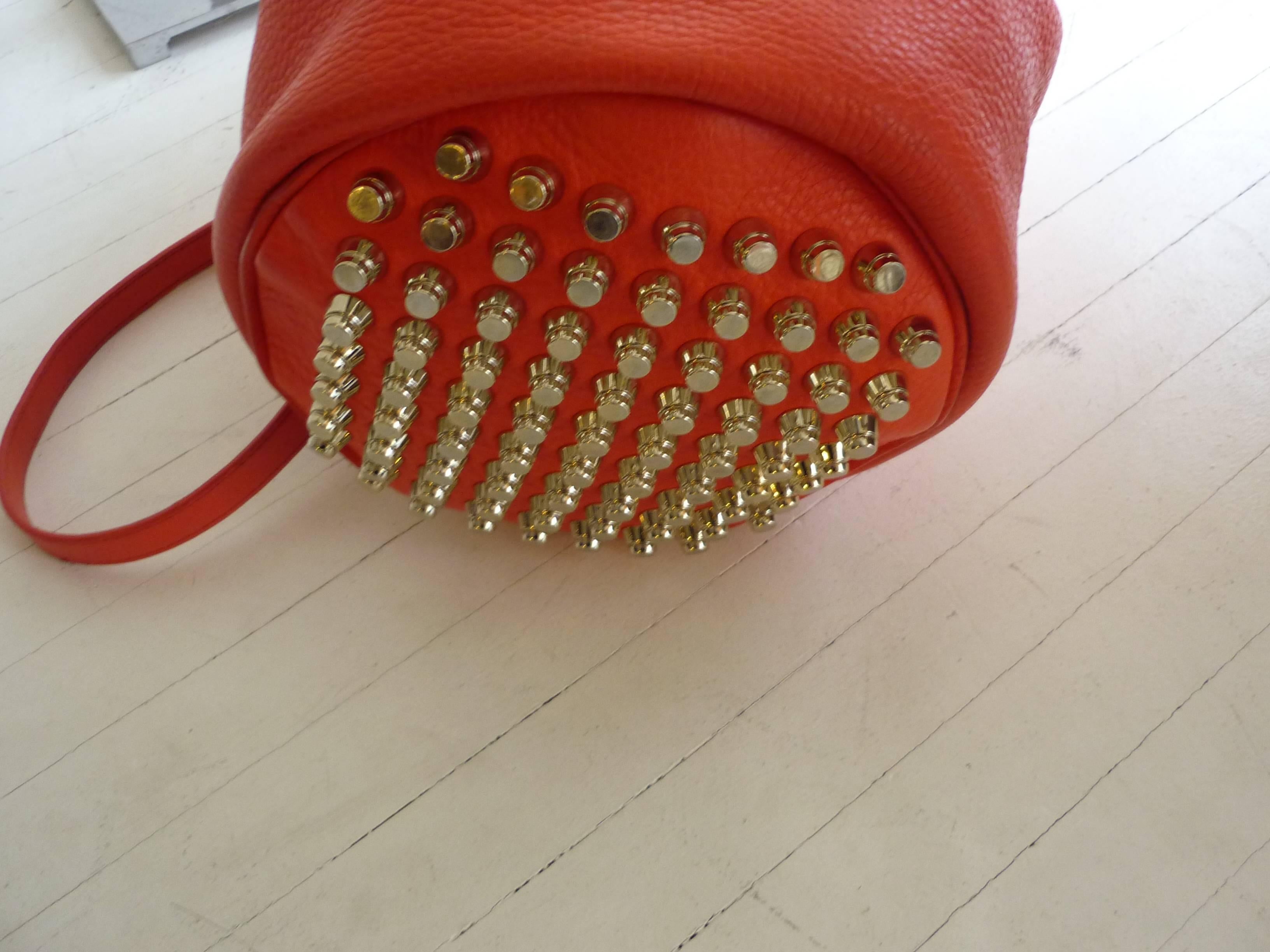 Lovely pre-owned condition, this bag is made of an orange/red pebbled leather. There is a top handle as well as an adjustable shoulder strap, and has a fully studded base as well as studding around the pleated front. 

There is an internal zipped