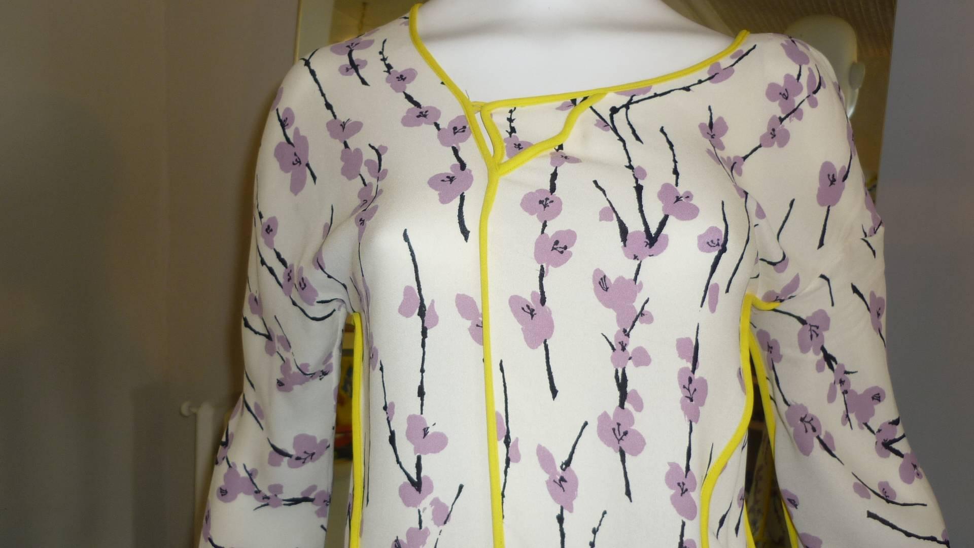 Can be worn as a tunic or mini dress this silk dropped waist dress has an ivory background, with purple flowers and black branches remeniscent of a Japanese screen painting. A bright yellow band runs troughout the piece, including the assymetrical
