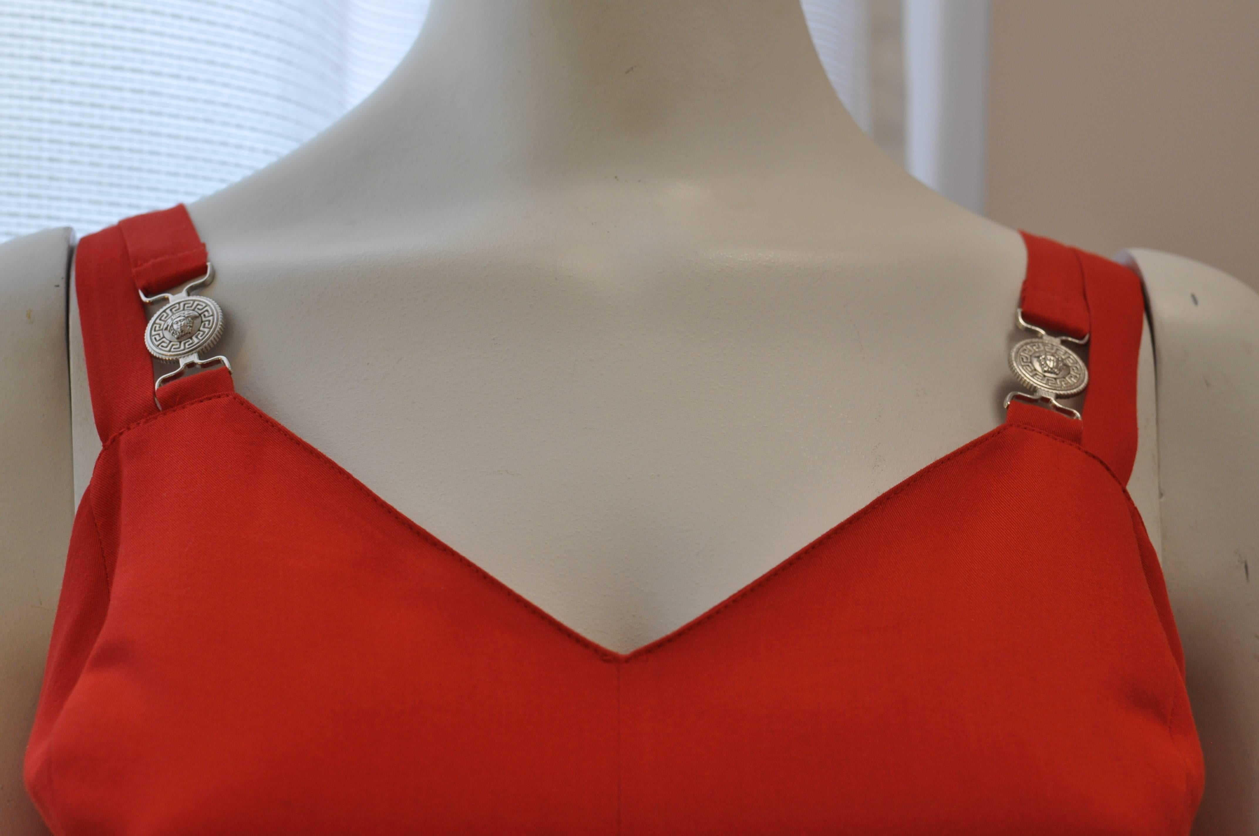 Nice A-line red dress with a v-neckline; pleated at the bottom and silver Medusa strap tabs front and back (with parallel plain straps). 

The material is viscose.