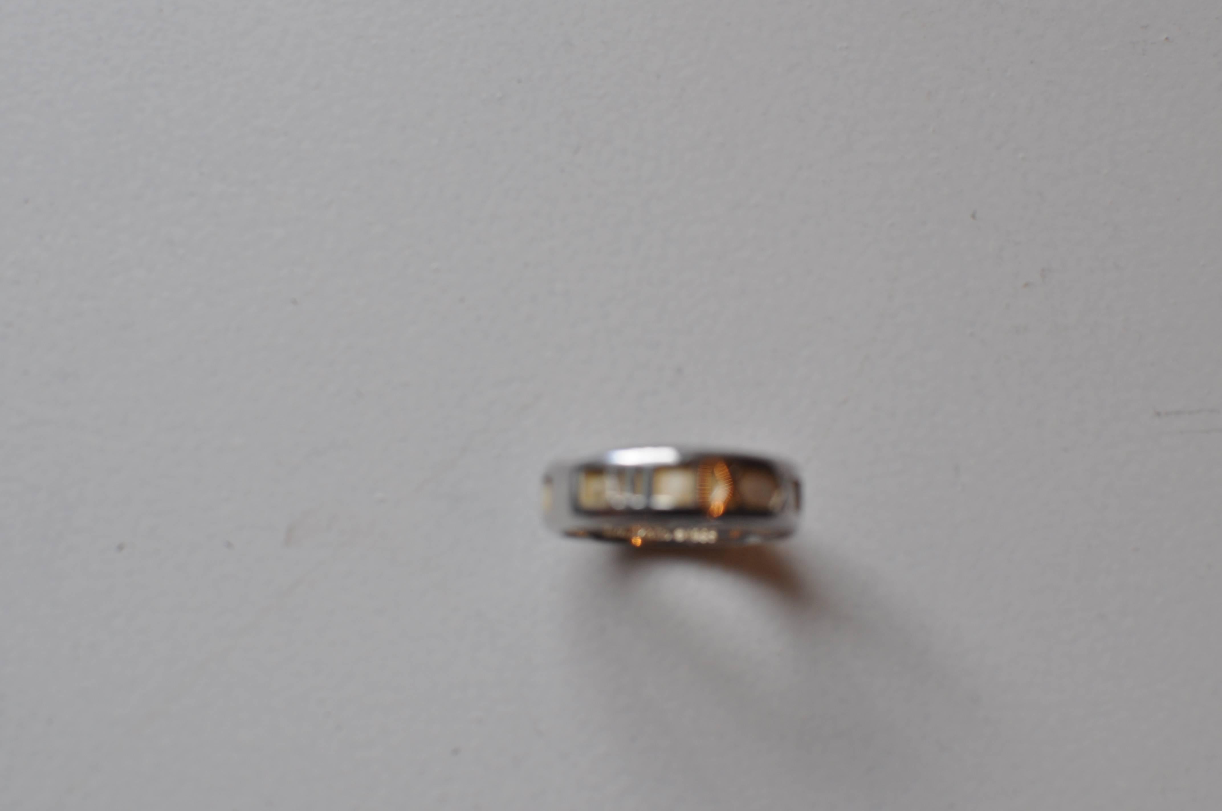 Would make a very nice present or wedding band. It is a 925 - Italy solid silver band. There is an inscription on the inside. The squares between the Roman numerals look like brushed gold.

Apart from the inscription the piece is marked Tiffany &