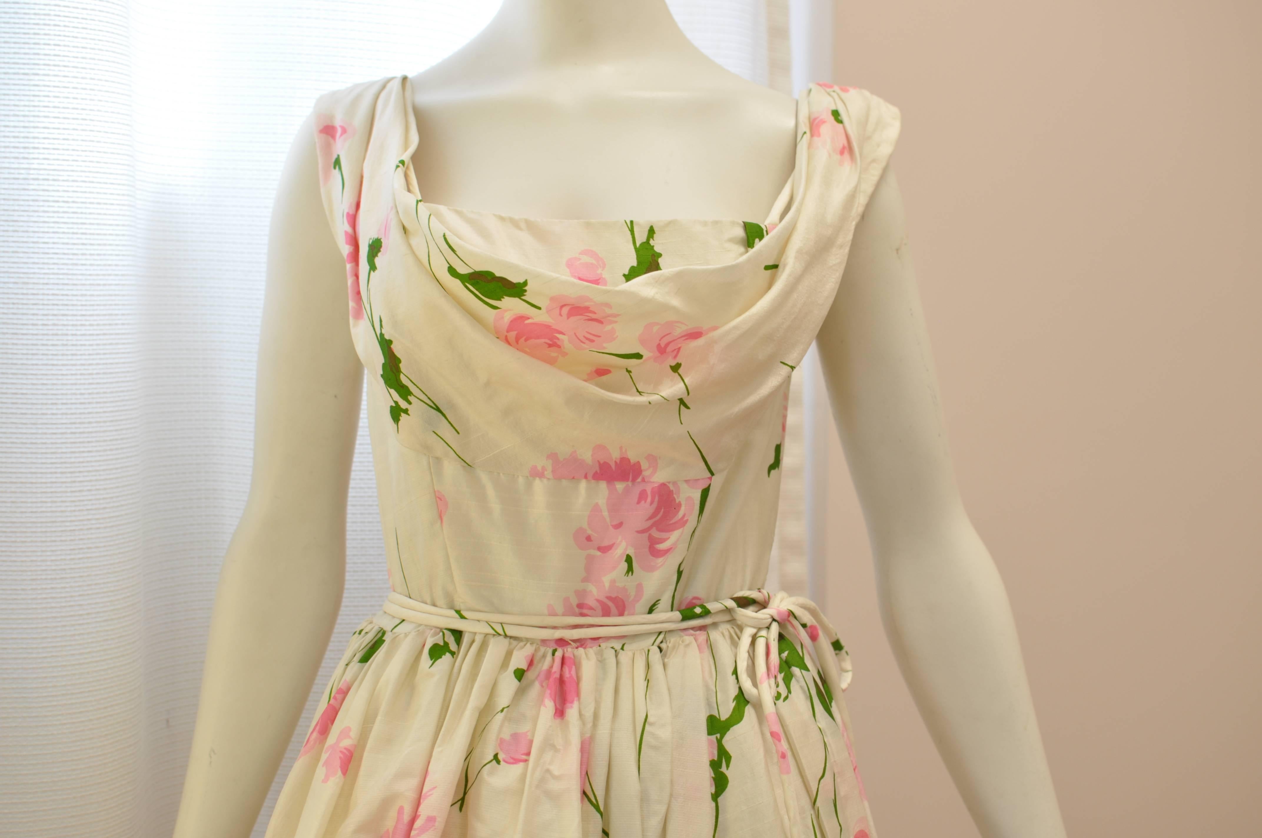 Tea dress or cocktail dress, this is a beautiful dress with a floral print on an ivory background. The fitted bodice has a double neckline one being a cowl, and there are also stays at the bust. The skirt is flared with the help of a stiff