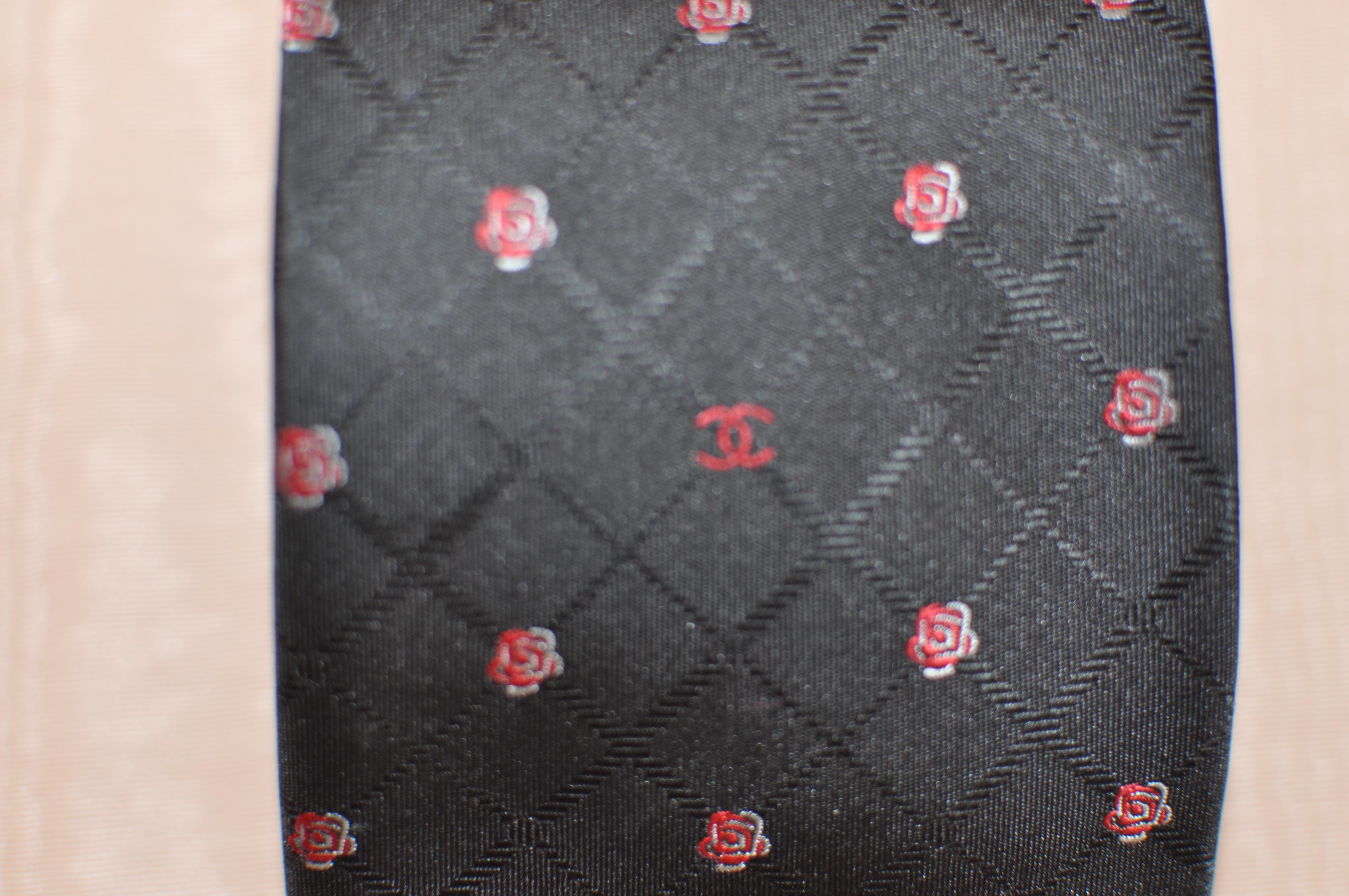 This tie has a black criss cross background with a nice white and red camellia print interspersed with the Chanel logo.