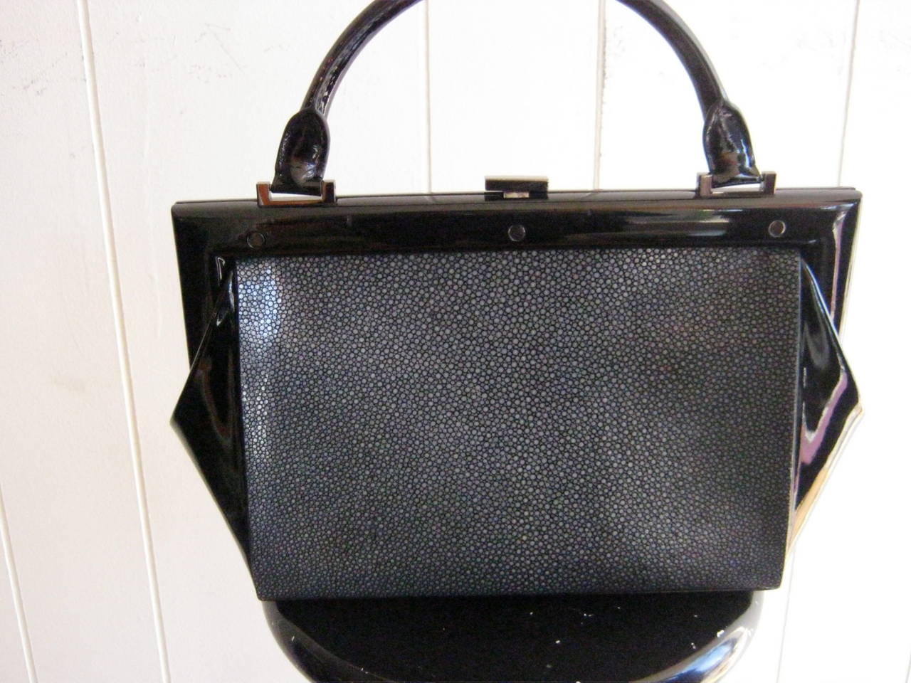 This structured stingray handbag has a wood frame, patent leather sides and handle, very soft lambskin lining, and two interior pockets. It is in perfect condition except for a couple of small chips on the wooden frame.

Closure is by a top clasp,