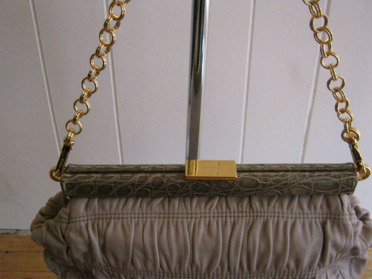 Can be a clutch or a bag, as the gold chain is detachable. There are two inside pockets with one zipped. The opening is by way of a gold clasp with Prada incised and a border of croc stamped leather.

This bag is in in pristine condition. Chain