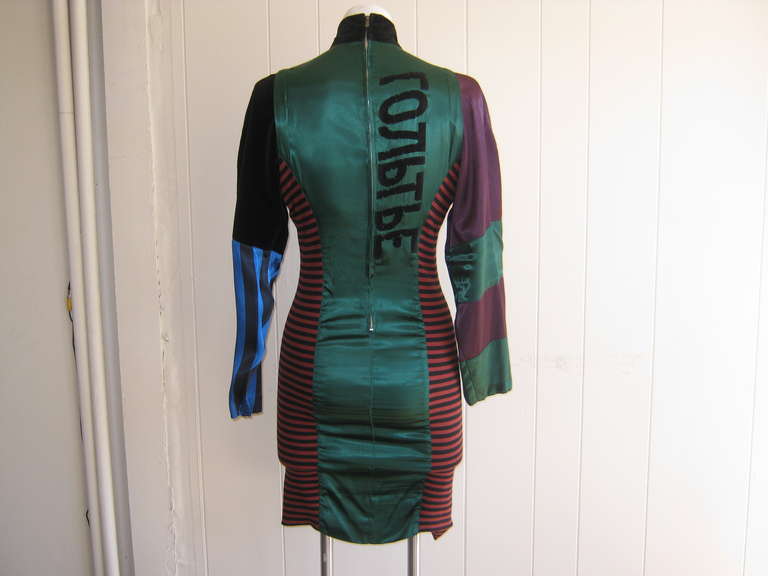 This dress is held in the Metropolitan Museum of Art Collection.It is made of green stretch satin with striped knitted sides which have a stretch, and flocked cyrillic script panels to the front and back. The dress sports a high velvet collar.The