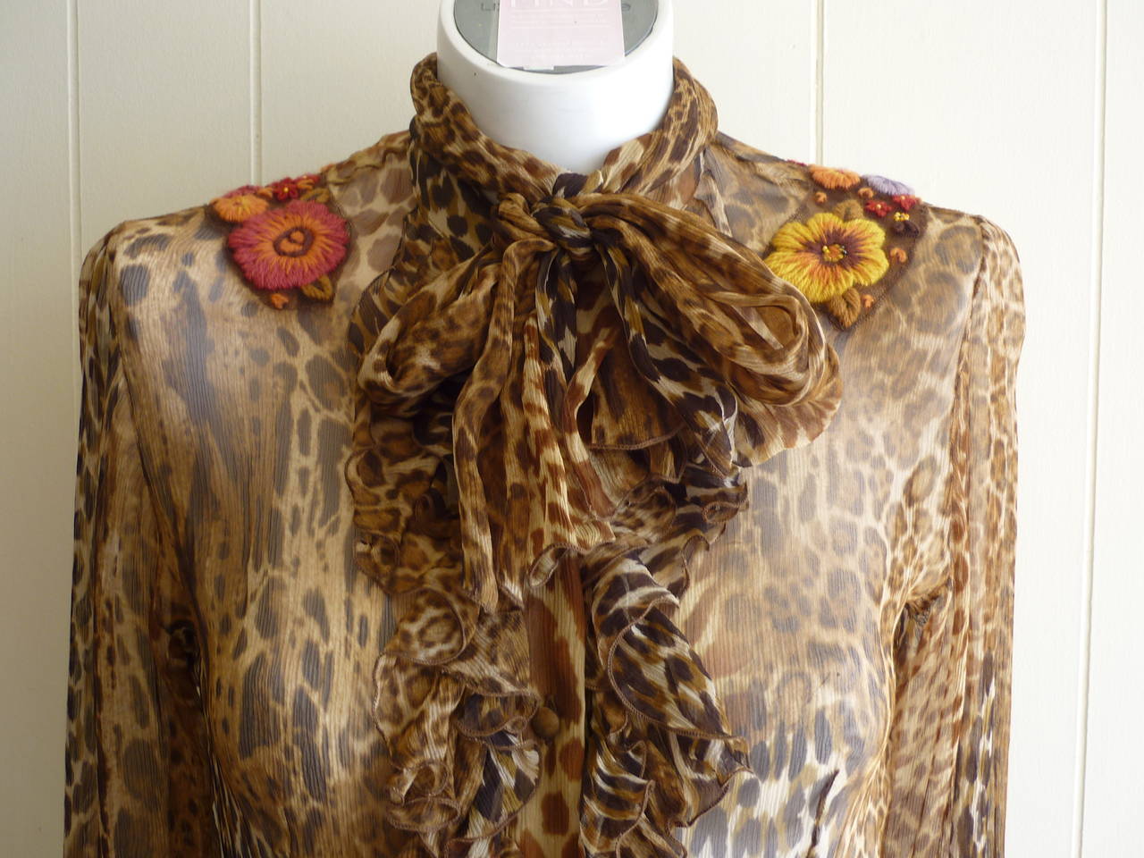 This leopard print silk chiffon blouse as great floral embroidery detail of wool on mesh on both shoulders, as well as ruffles down the front and an attached scarf.

The covered buttons are found down the front of the blouse and on the cuffs.