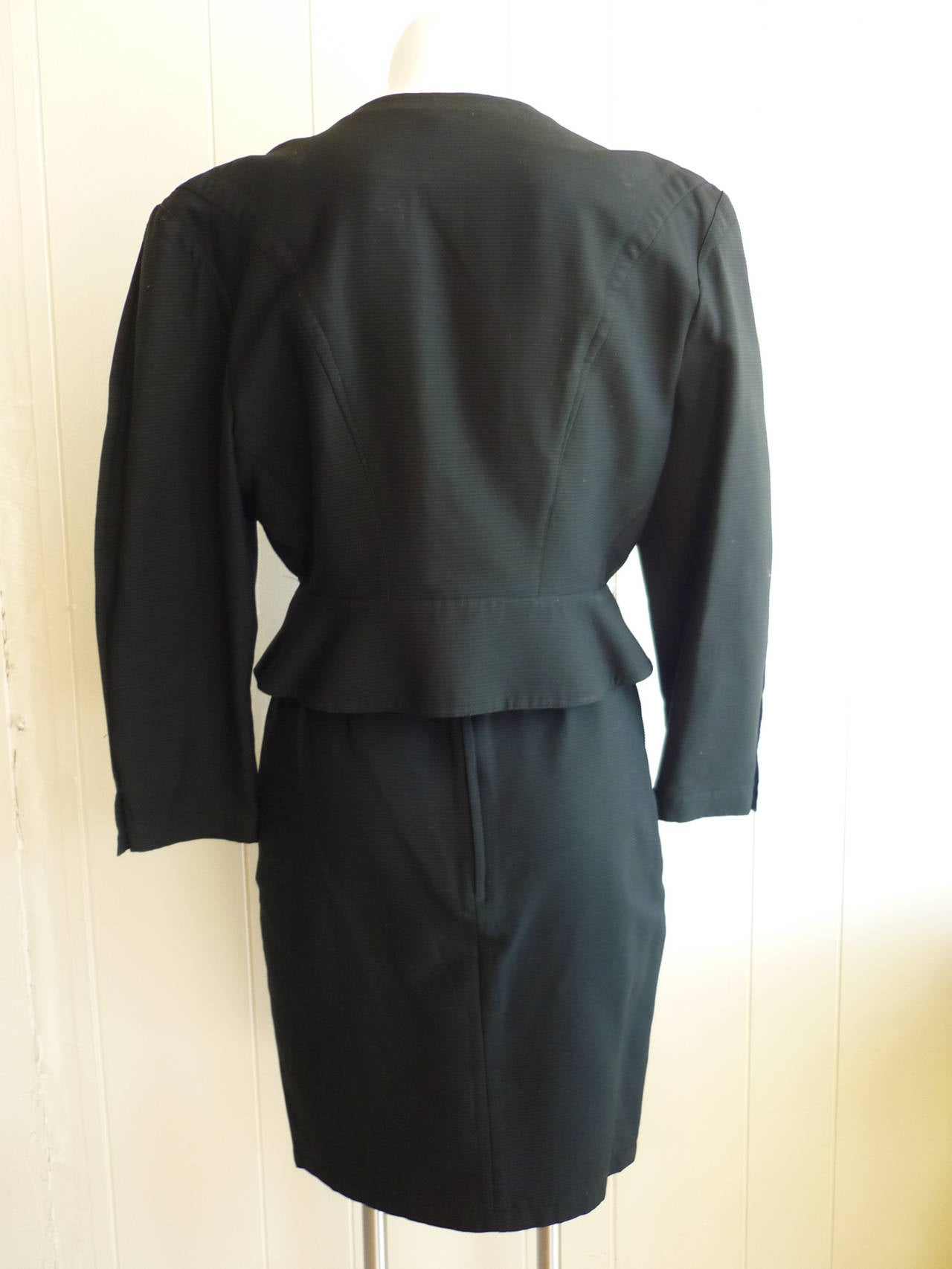 Very recognizable as a Mugler piece, this suit has snap buttons; exaggerated shoulders; a v-neck; peplum type jacket; darts galore, and a skirt with a front double pleat.

Skirt measurements: length 23