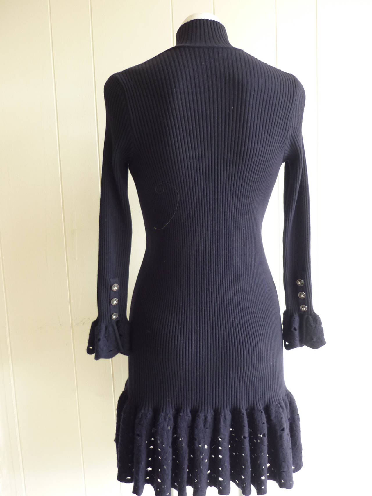 Absolutely beautiful dress of ribbed wool, it has a high collar and ten rare white elephant buttons from the neck to the bottom of the dress. But that is not all, the cuffs and hems are wool crochet, and the cuffs each sport three white elephant