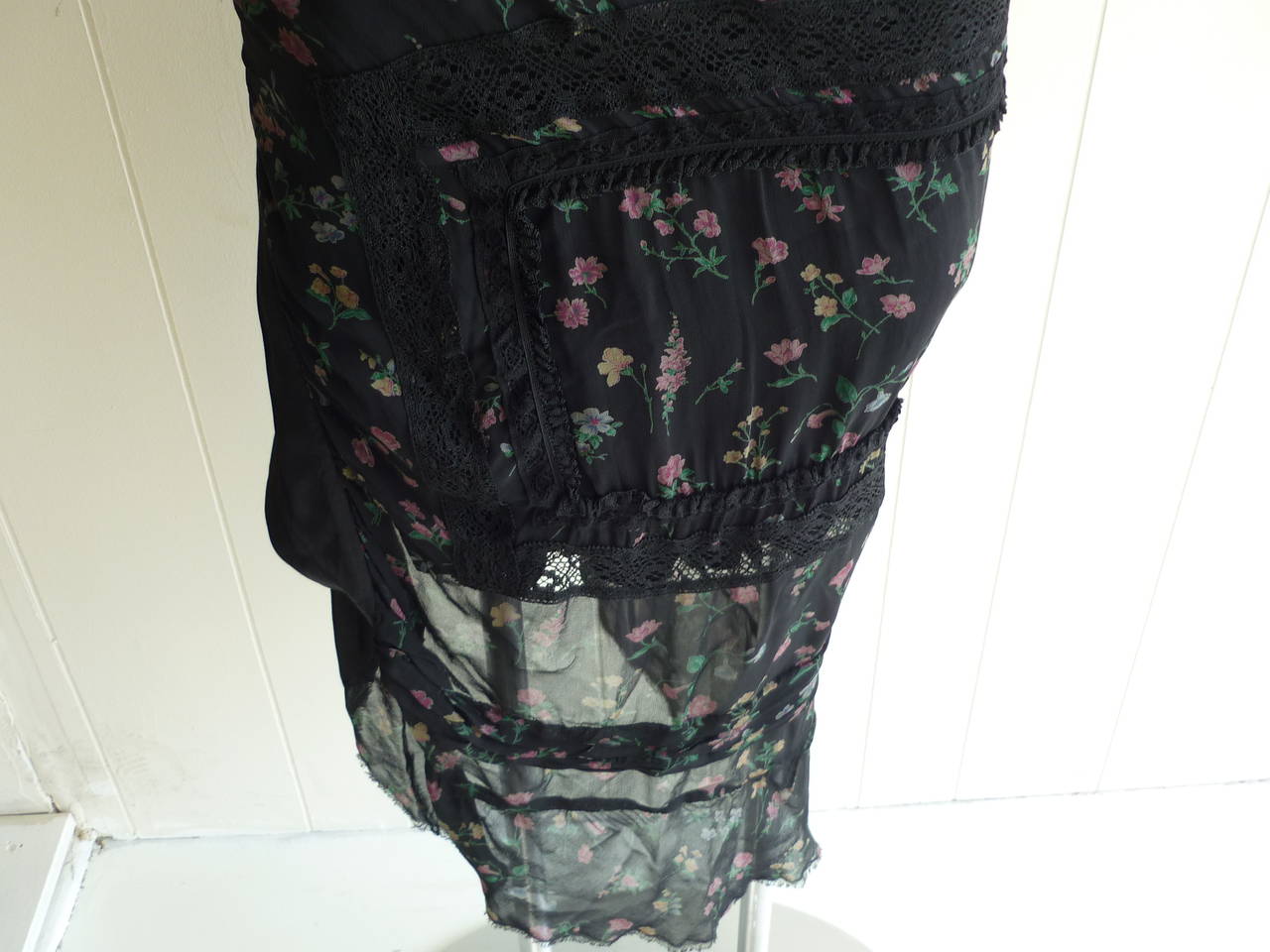 An intricate piece to describe! The skirt is made of 100% rayon. There is an underskirt in solid black and a longer over skirt with a floral pattern, lace trim, stitched pleats and ragged hem.

In addition, the overskirt does not go around but
